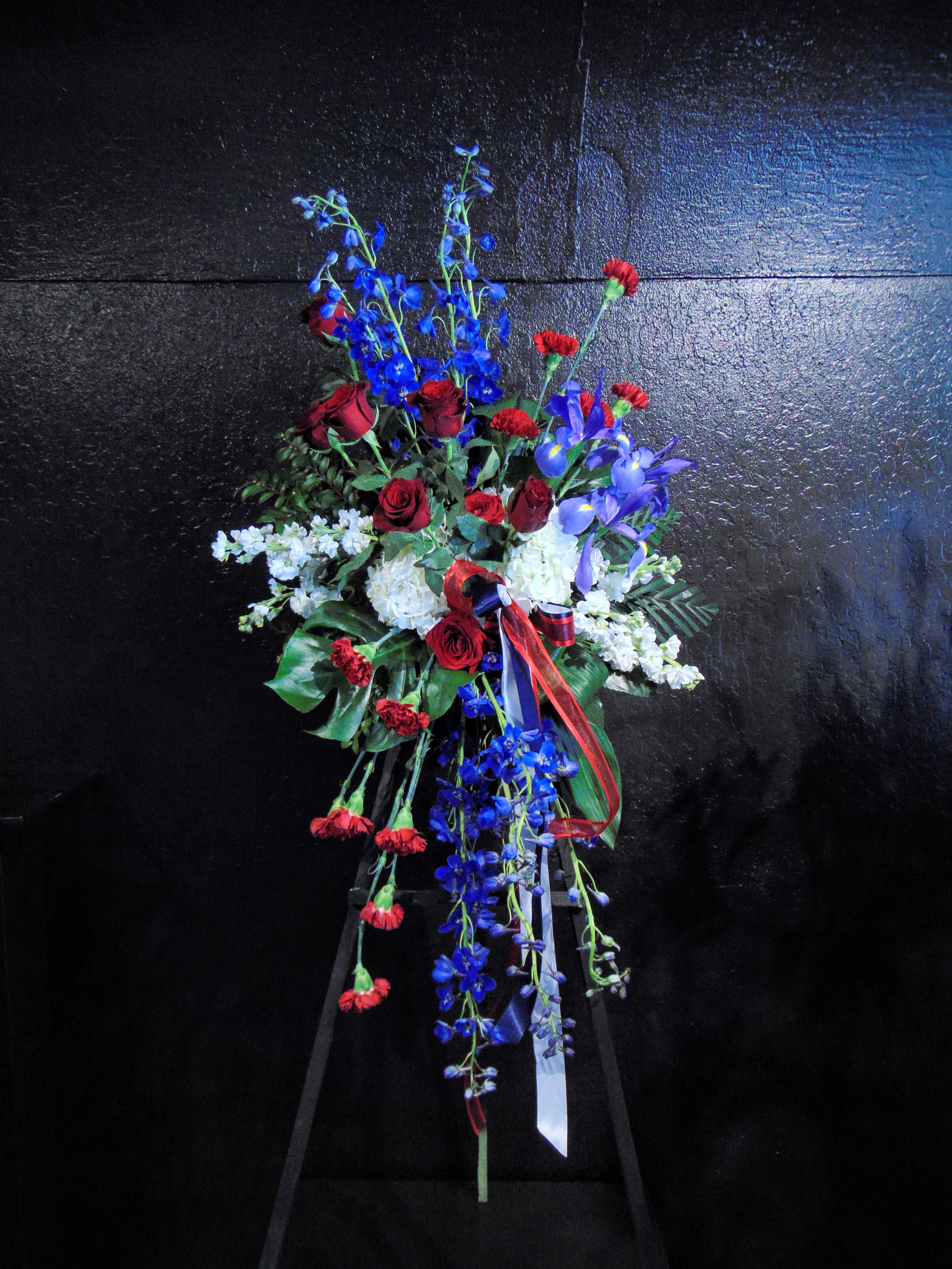 Standing spray of red roses and carnations with blue delphinium and white flowers on an easel