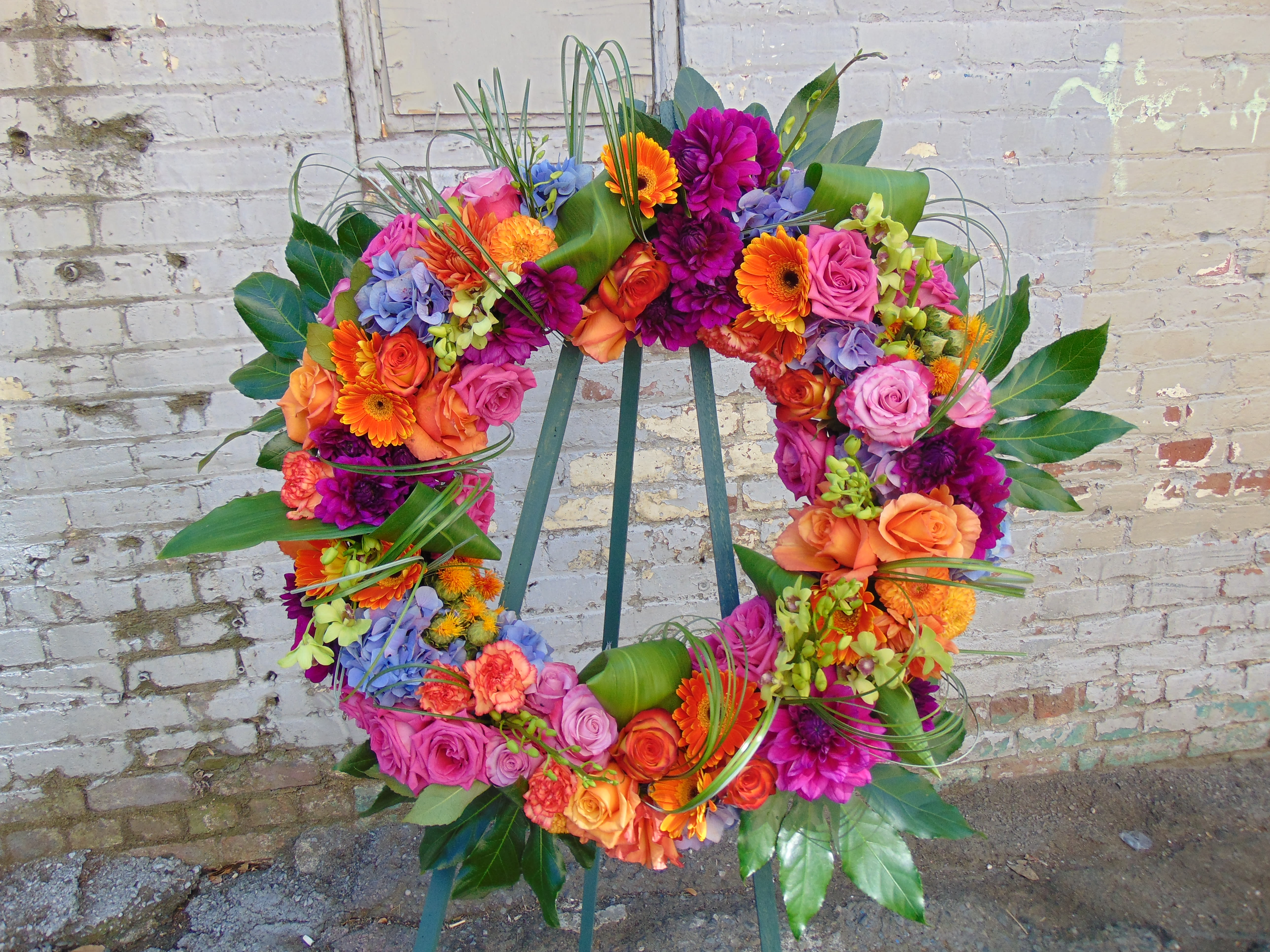 Bright circular wreath of orange, pink, and purple flowers displayed on a metal stand.