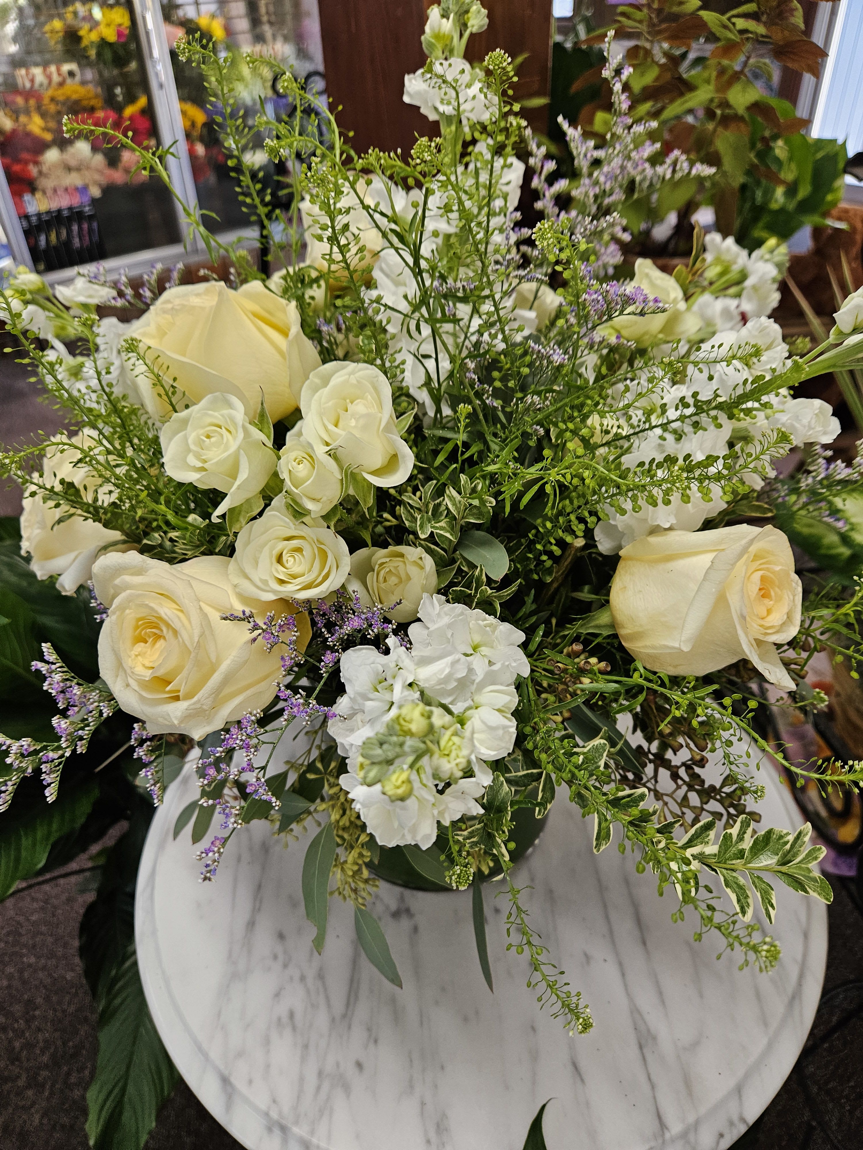 Vase arrangement of cream roses and white flowers with airy greenery on a round marble table