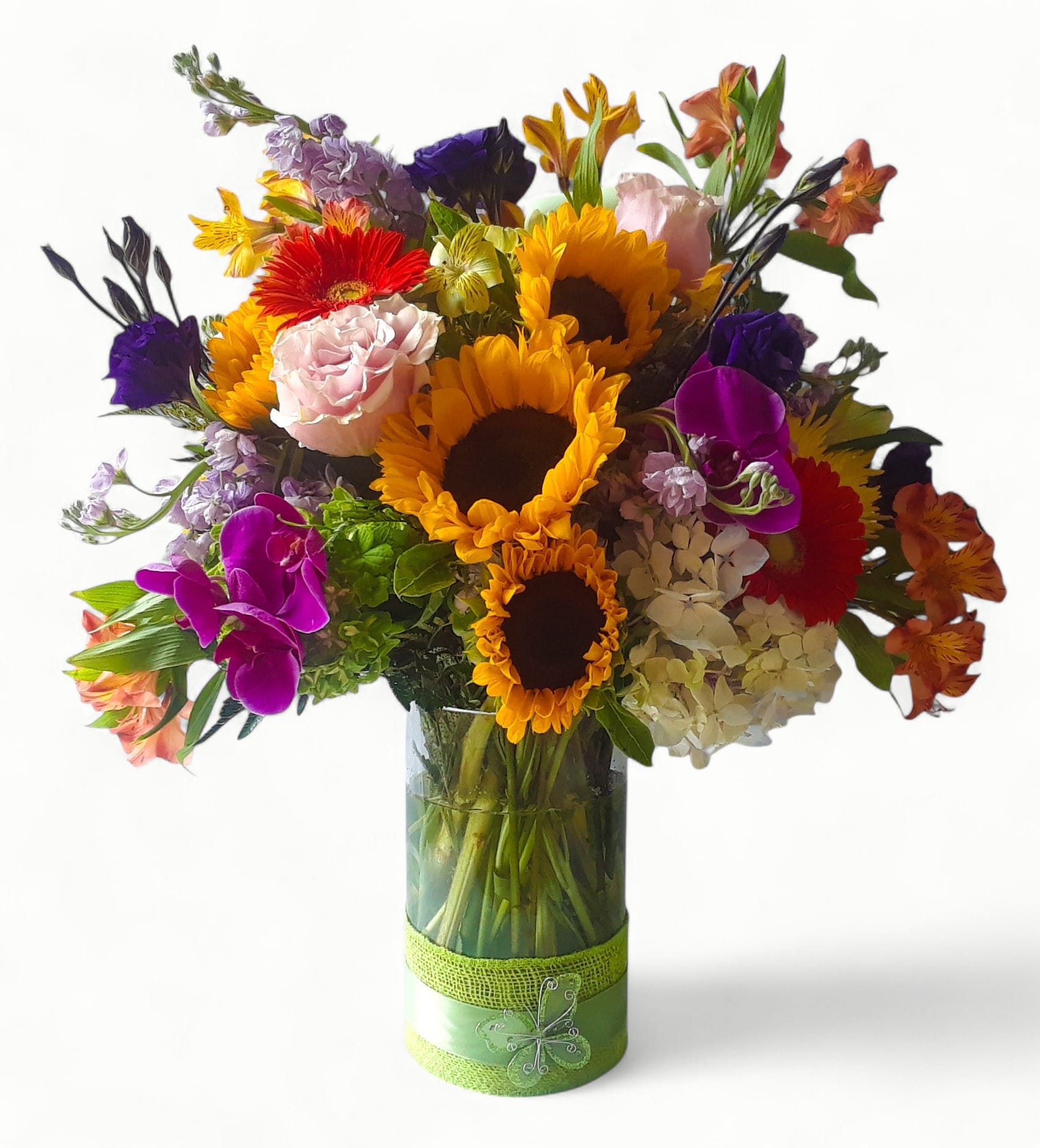 Tall mixed arrangement with sunflowers, roses, gerbera daisies and orchids in a clear glass vase with green ribbon