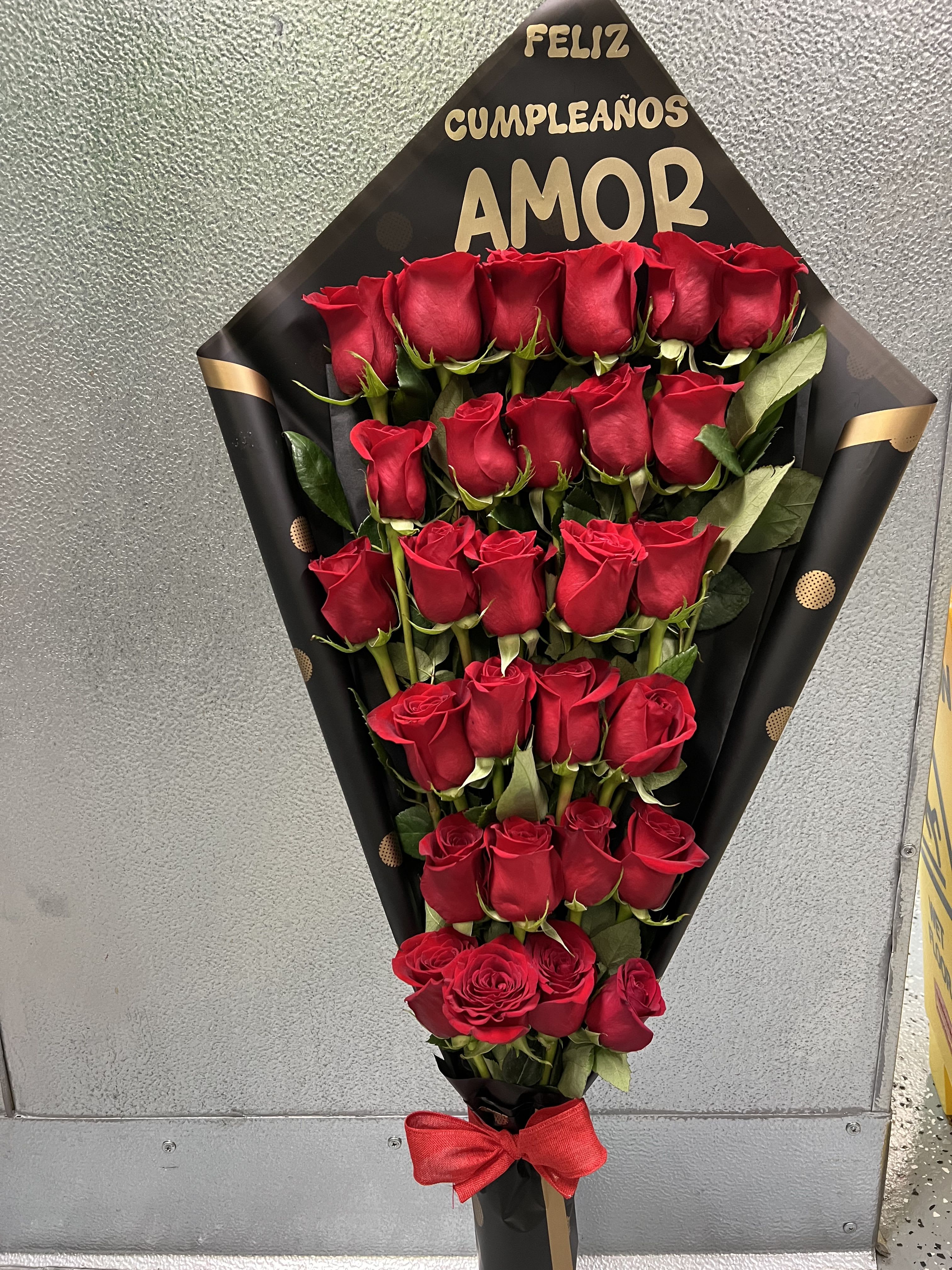 Tall bouquet of red roses arranged in rows in black wrap with gold lettering and a red bow