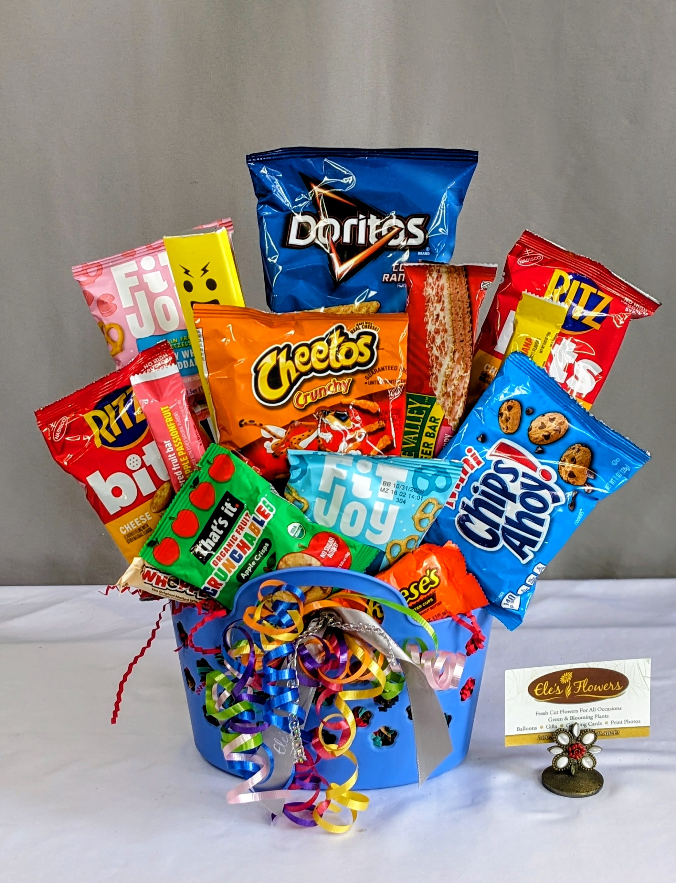 Yummy Snack Basket  - This fun and vibrant snack basket is packed with a delicious assortment of sweet and savory treats, making it the perfect pick for any occasion. Arranged in a colorful container and accented with playful ribbon curls, it offers a satisfying mix of crunchy, chewy, and indulgent goodies to please every craving. Whether you’re celebrating, sending a thoughtful gift, or simply treating someone special, this eye-catching basket delivers a little bit of everything to enjoy and share.  Container and snack offerings may vary from photos.   Standard - Approximate 15 - 18 pieces 