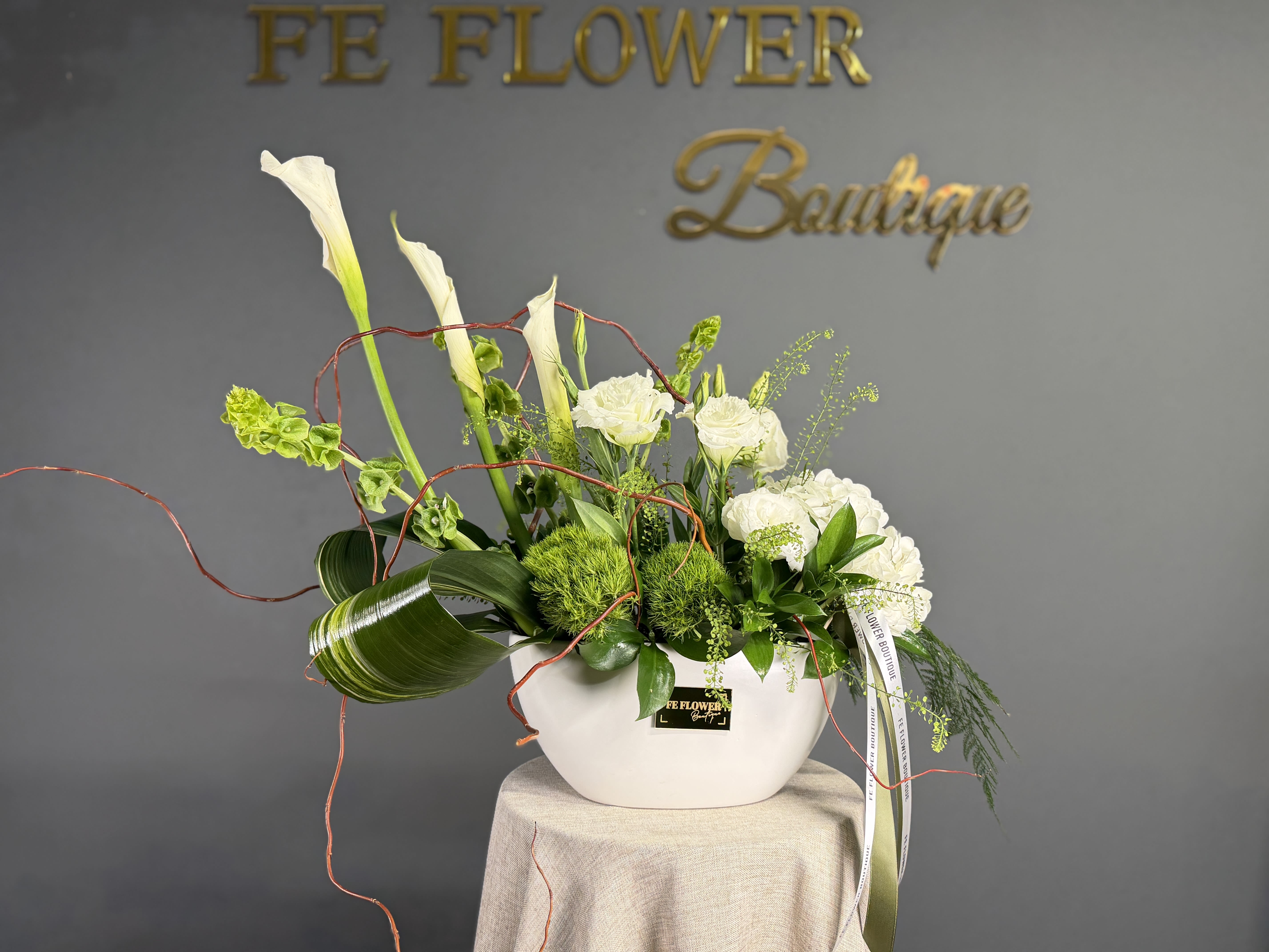 Modern white and green floral arrangement with calla lilies and roses in a low white ceramic bowl