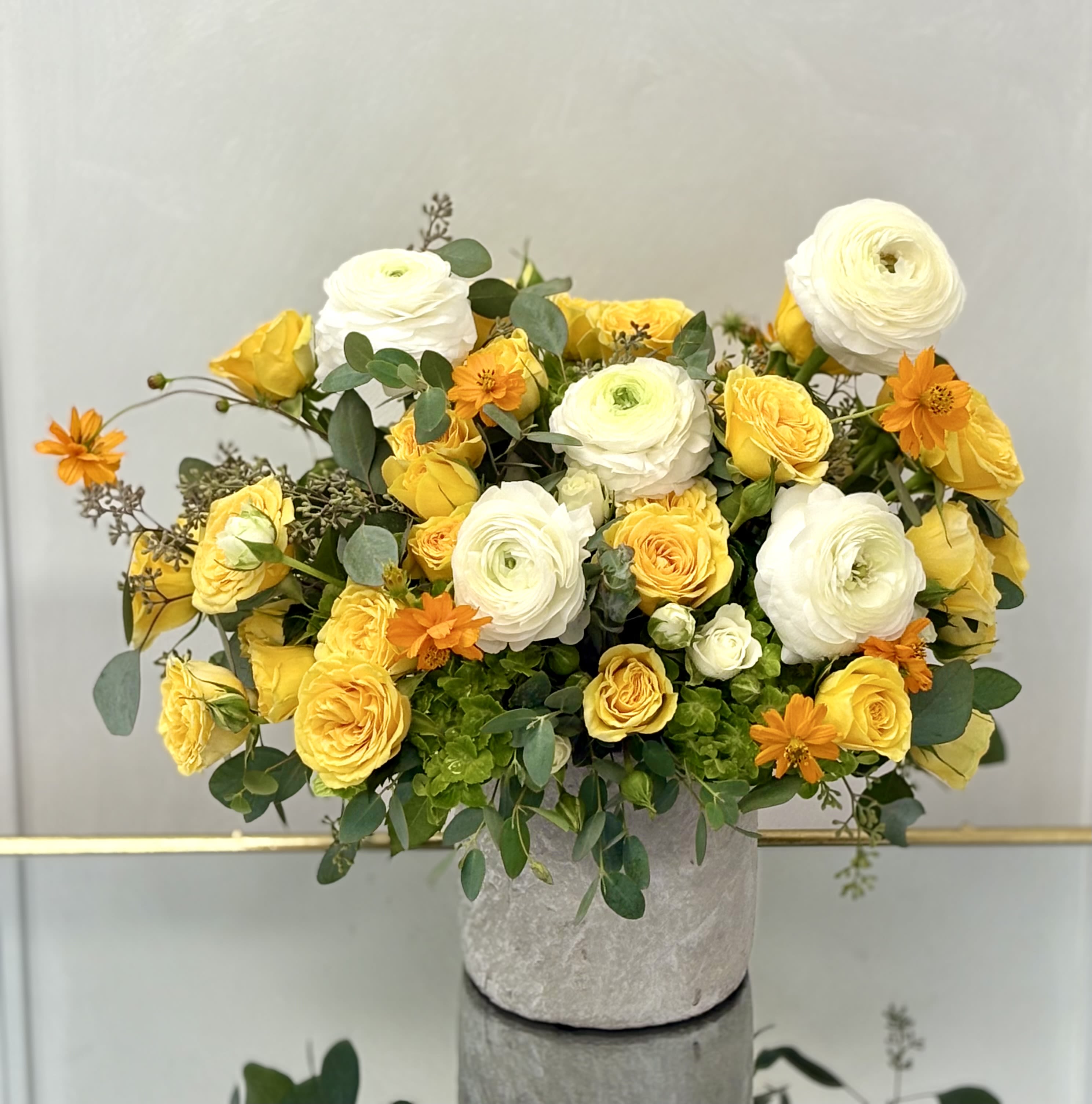 Yellow and white flower arrangement with orange accents in a gray stone pot