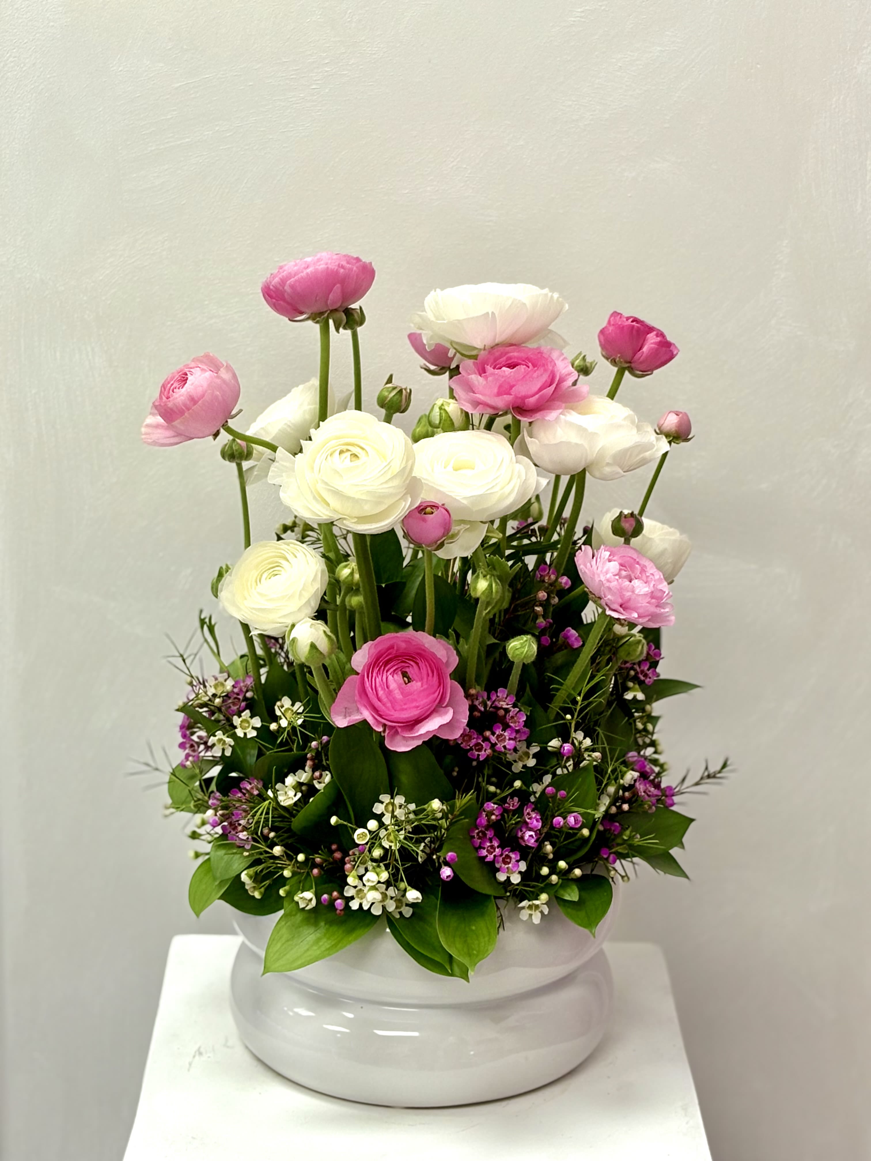 Pink and white ranunculus arrangement in a white ceramic bowl with small purple accent flowers