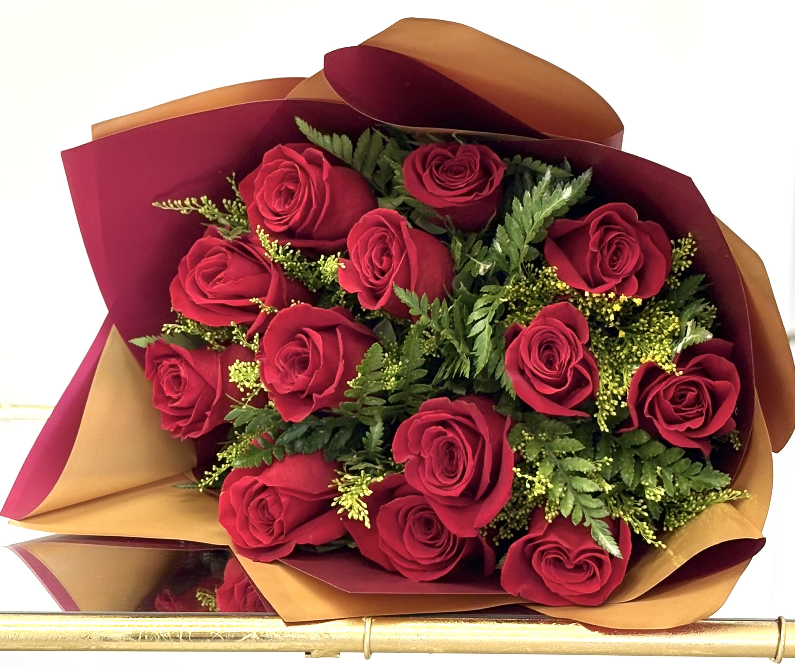 Hand-tied bouquet of red roses with fern accents wrapped in burgundy and gold paper
