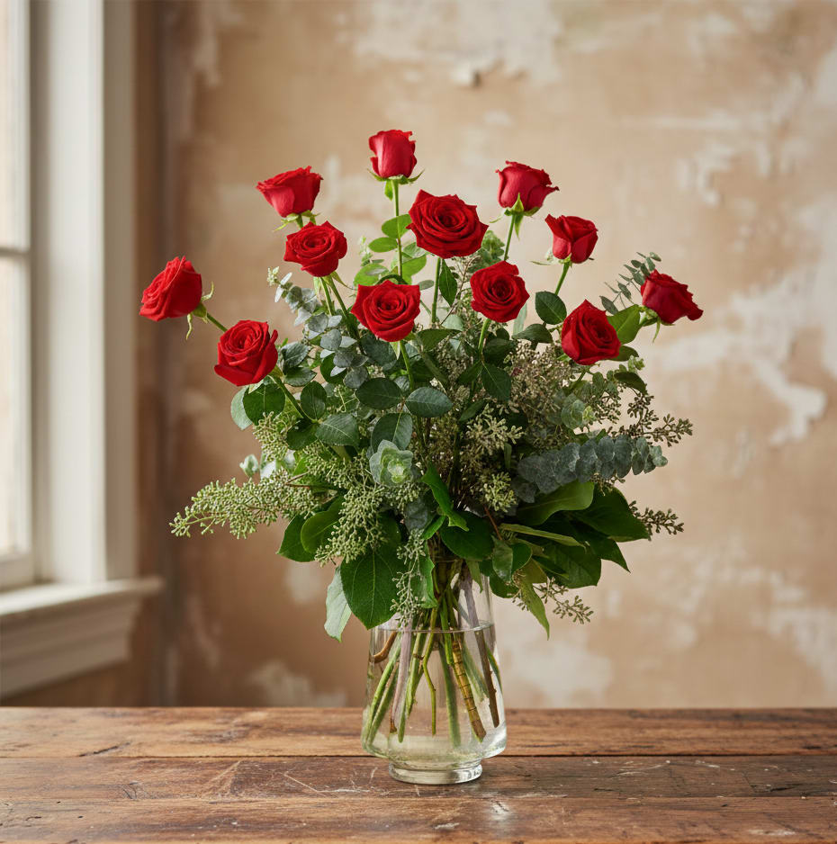 Tall bouquet of red roses with abundant greenery arranged in a clear glass vase.