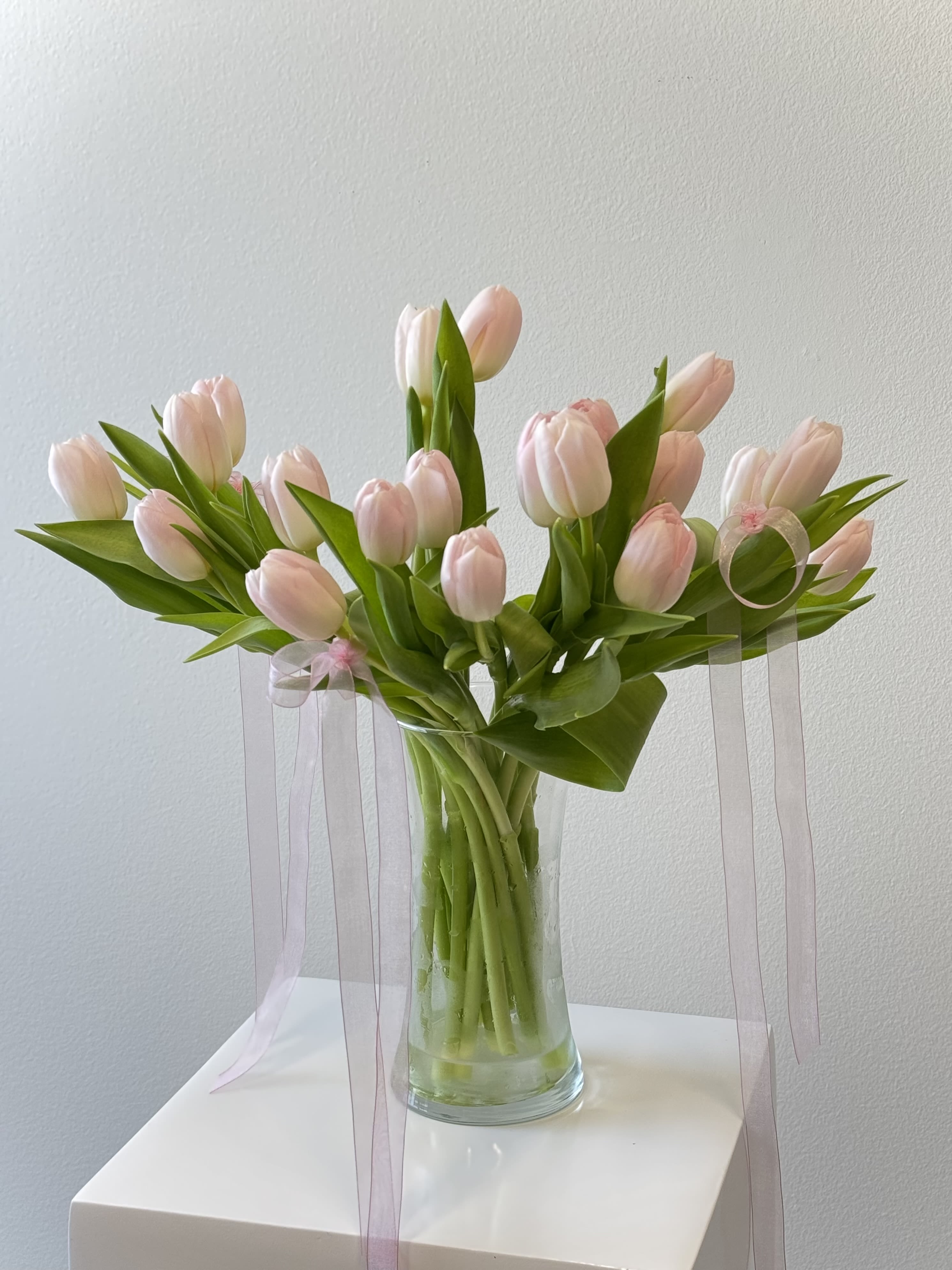 Arrangement of pale pink tulips in a clear glass vase with long sheer pink ribbons