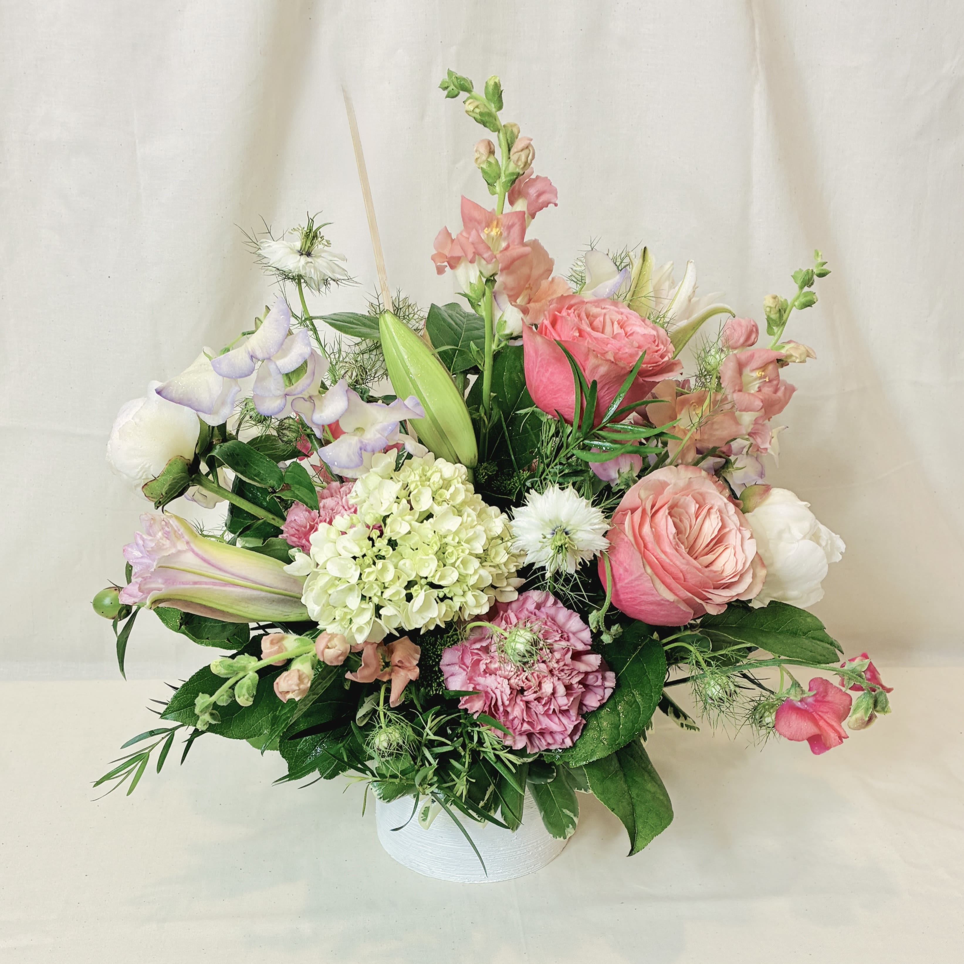 Pastel arrangement of pink roses, lilies, hydrangea and mixed blooms in a white cylinder vase