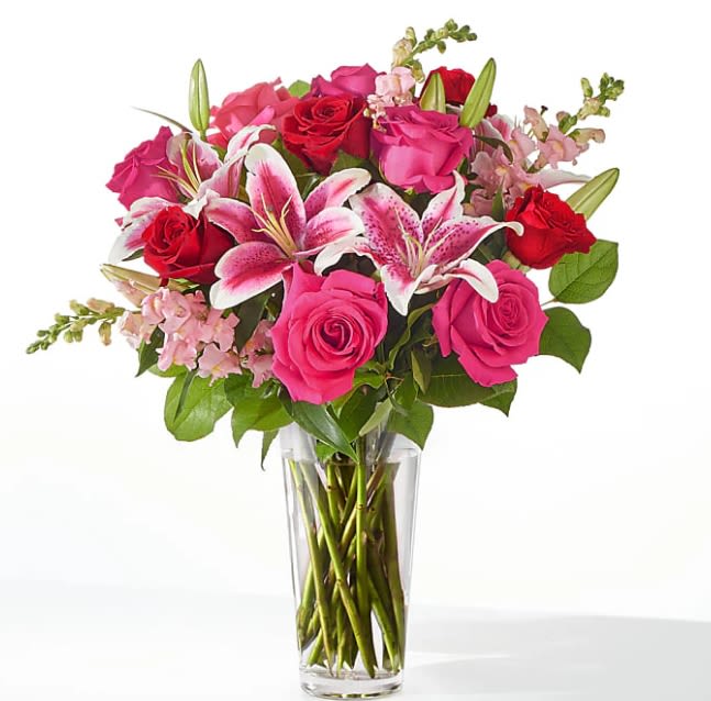 Tall glass vase of red and hot pink roses with pink lilies and snapdragons.