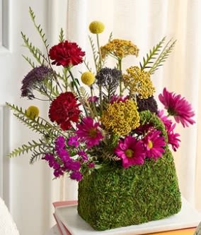 Colorful mixed flower arrangement in a moss-covered square container