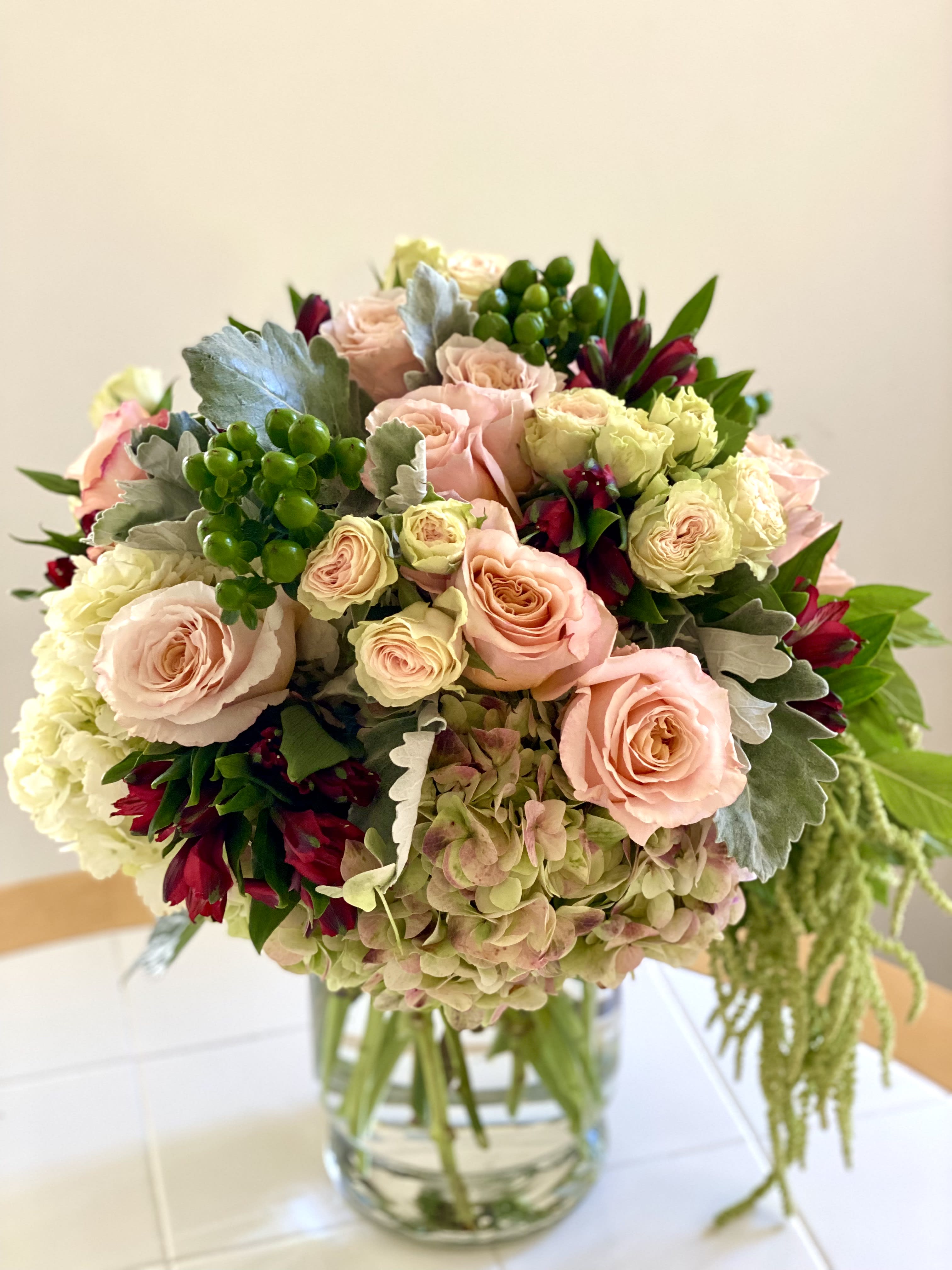 Round arrangement of blush roses, hydrangeas, and red flowers in a clear glass vase