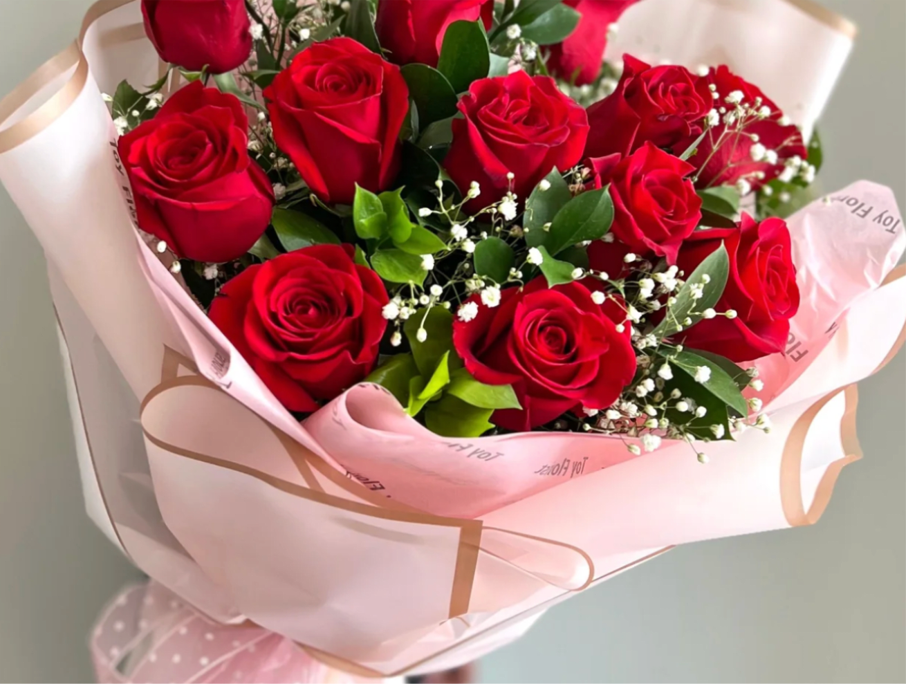 Bouquet of red roses with white filler flowers wrapped in pink paper