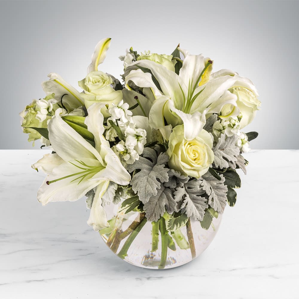 Low arrangement of white lilies and cream roses in a clear glass bowl vase