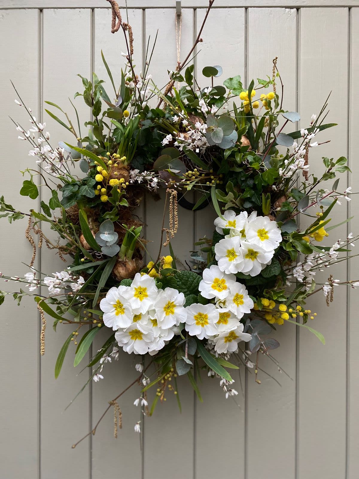 Spring wreath with white and yellow flowers and wild branches on a light gray paneled door