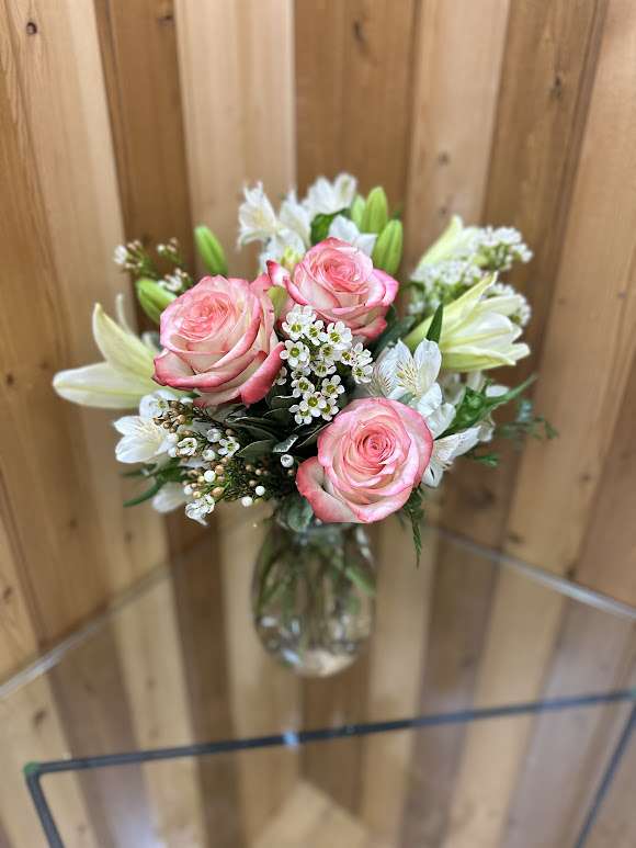 Pink roses and white lilies with small white blossoms arranged in a clear glass vase.