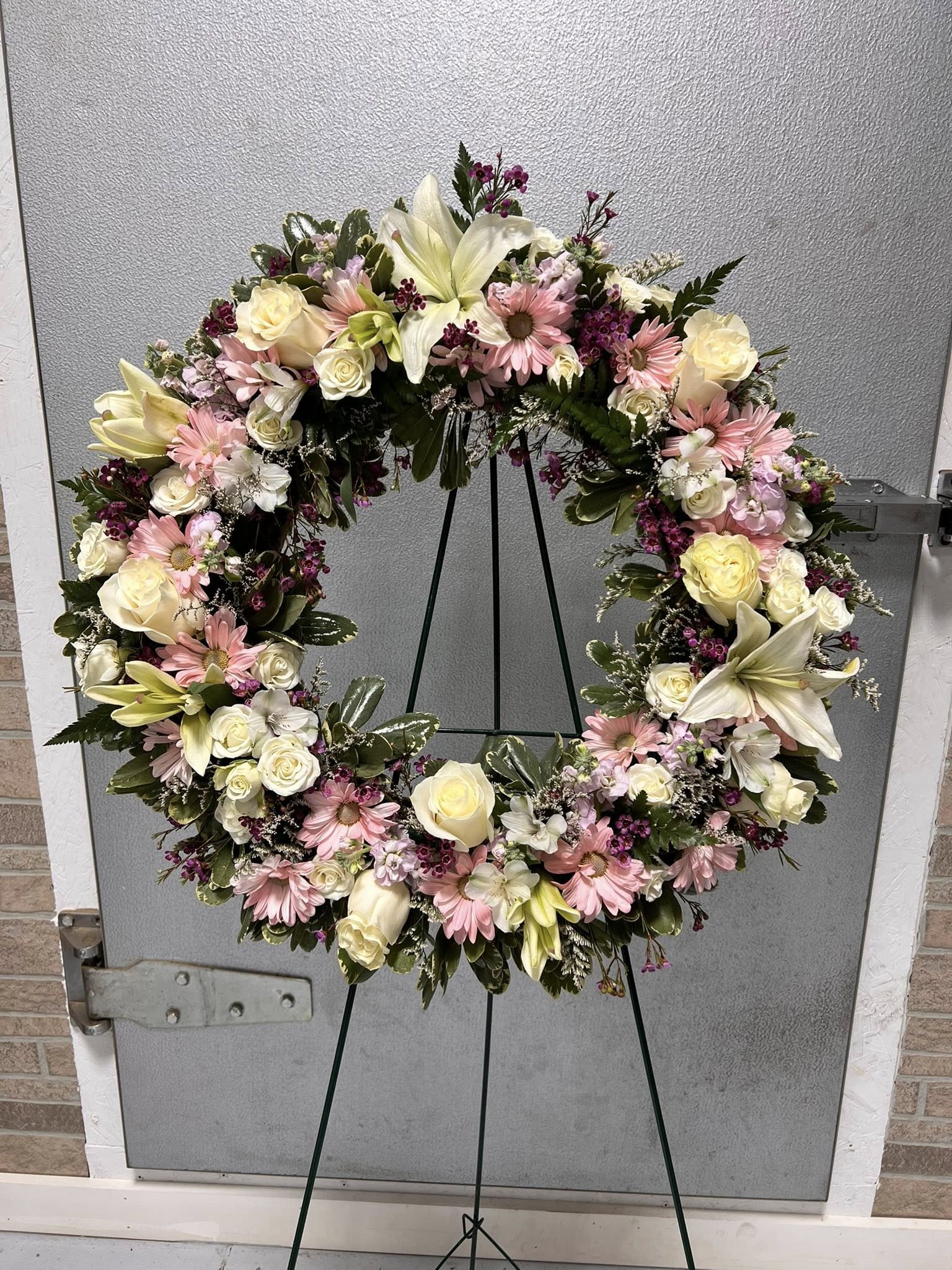 Standing wreath of pink daisies, white roses, and lilies on a green easel.