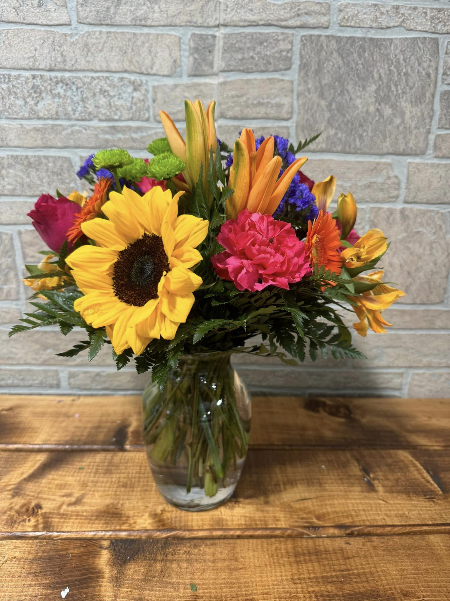 Bright mixed bouquet with sunflowers, lilies, carnations and other blooms in a clear glass vase