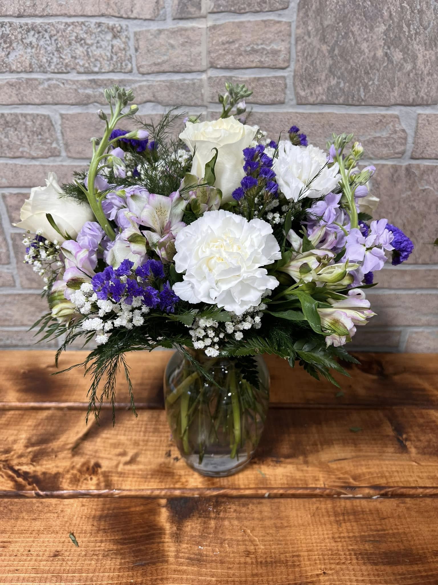 Mixed bouquet of white and purple flowers in a clear glass vase on a wooden surface