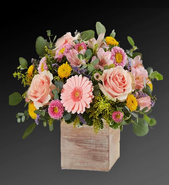 Pastel pink and yellow flower arrangement in a rustic wooden cube container