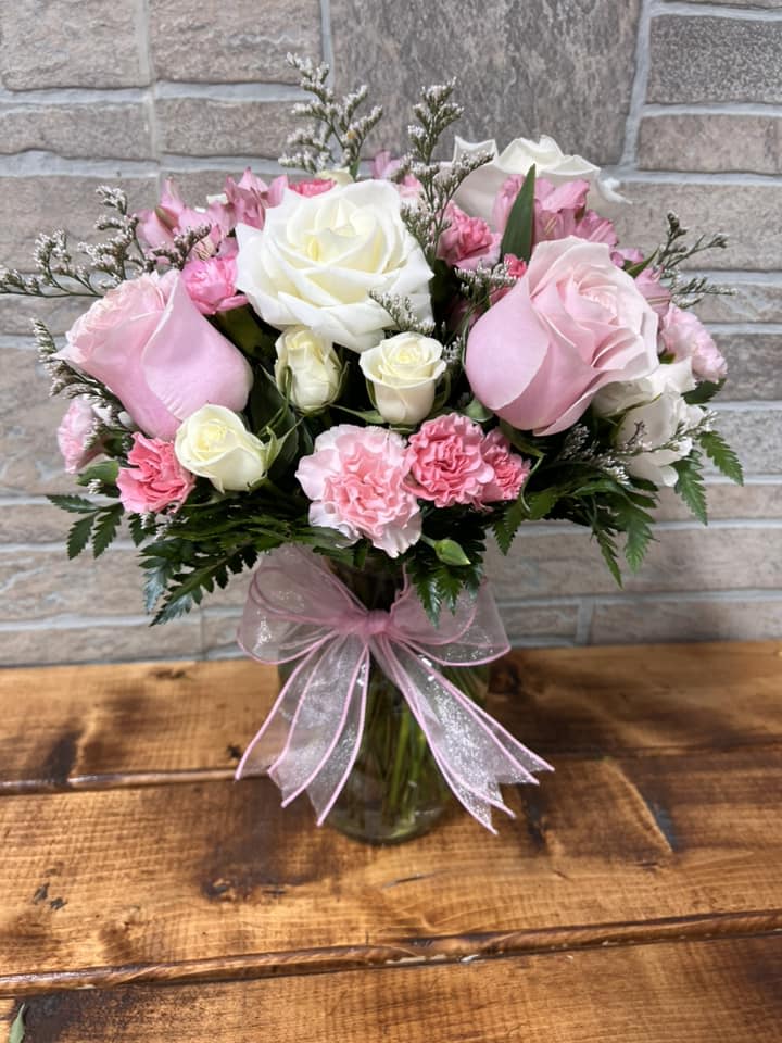 Pink and white roses with pink carnations in a clear glass vase tied with a pink ribbon bow