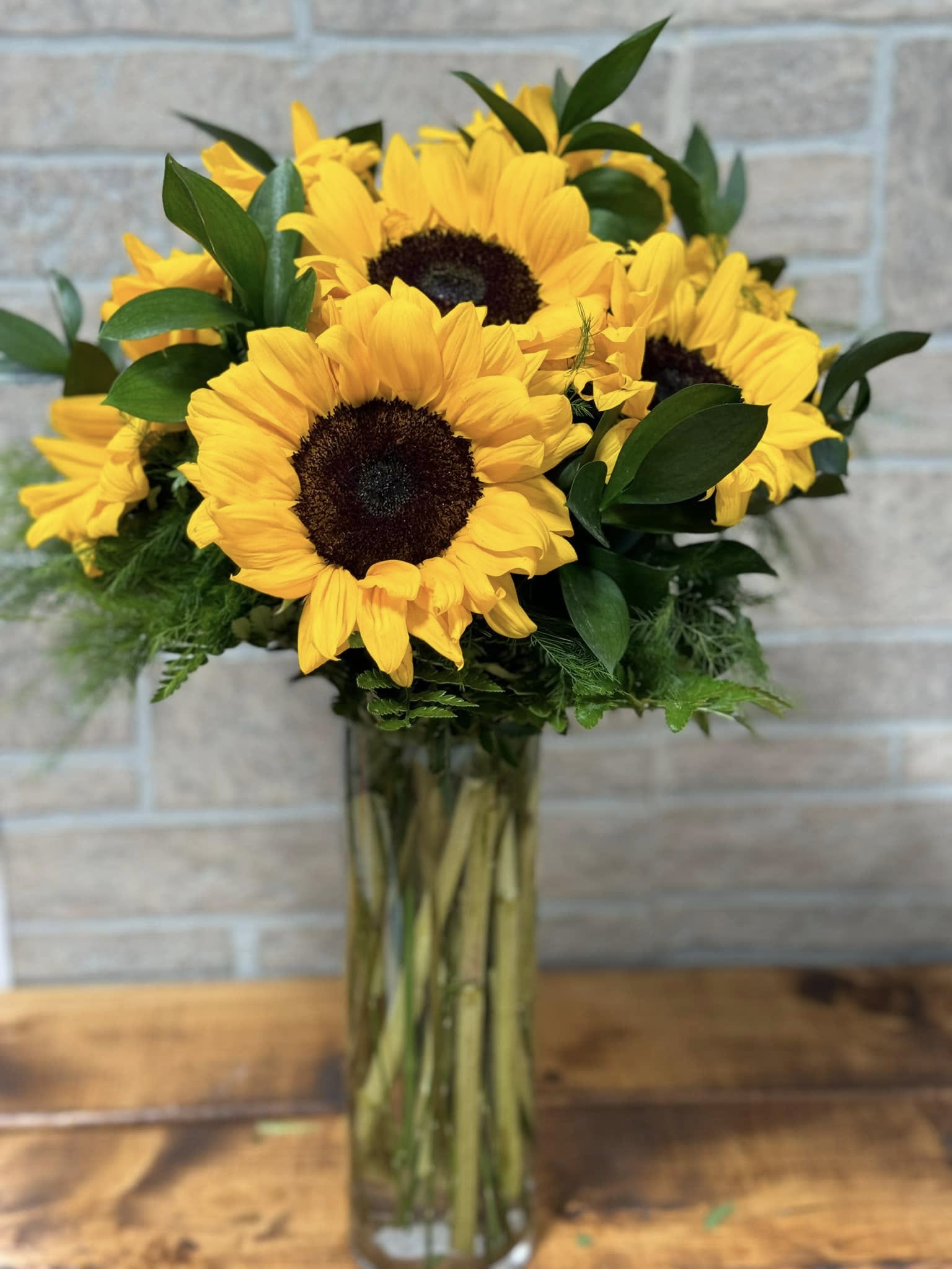 Tall glass vase of large yellow sunflowers with dark centers