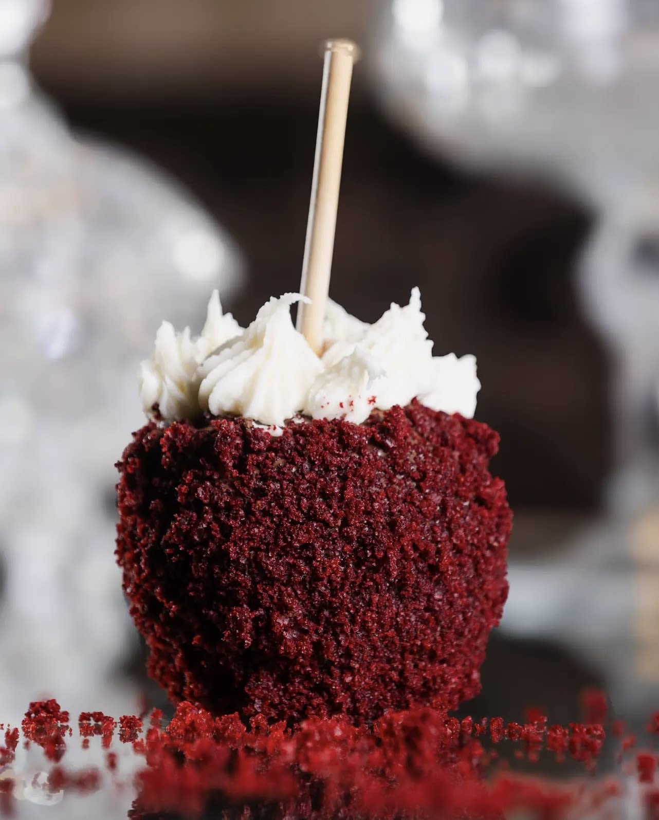 Red velvet cake pop coated in crumbs with white frosting and a wooden stick