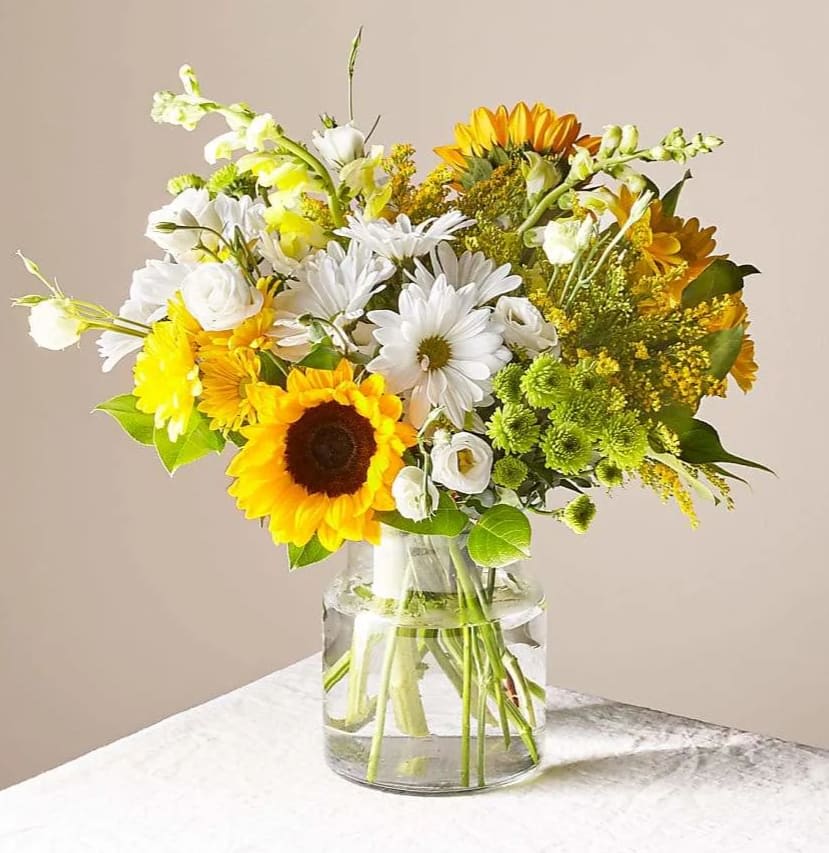 Mixed bouquet of sunflowers, white daisies, and yellow blooms in a glass vase