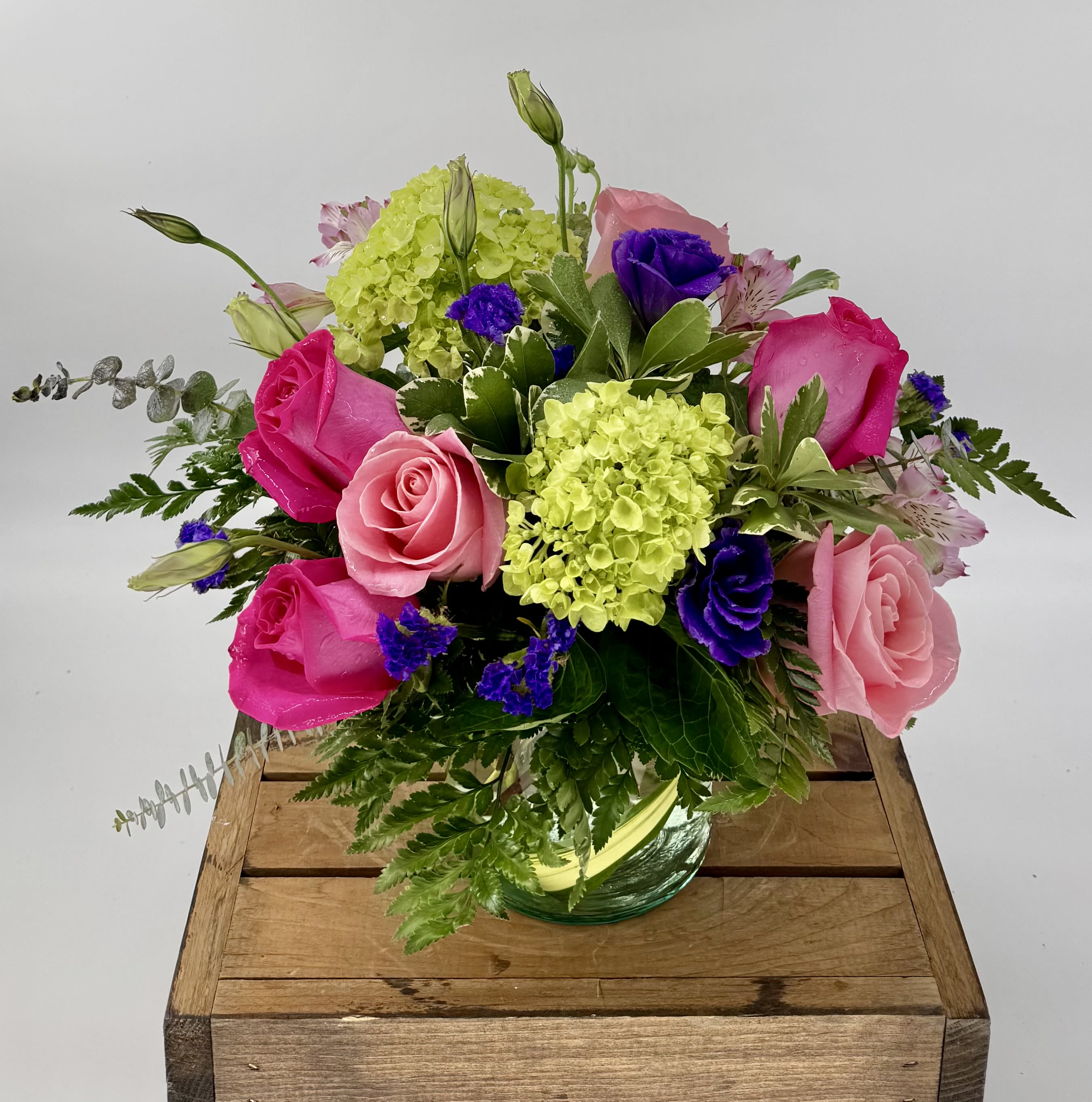 Spring Fling (DL) - Vibrant flower arrangement featuring hot pink and soft pink roses, lush green hydrangea, delicate lisianthus, and purple statice, elegantly displayed in a chic 5x5" clear cylinder vase. 