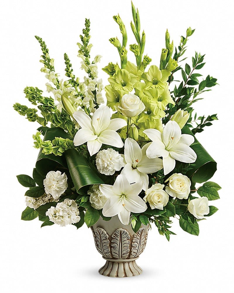 Teleflora's Clouds Of Heaven Bouquet - Peaceful and majestic in a large antiqued pot this wondrous white arrangement is a touching tribute to a bright life and your unending support. White roses white asiatic lilies green gladioli white carnations bells of ireland white snapdragons and white stock are accented with myrtle green ti leaves and lemon leaf. Delivered in a Thoughtful Tribute pot.