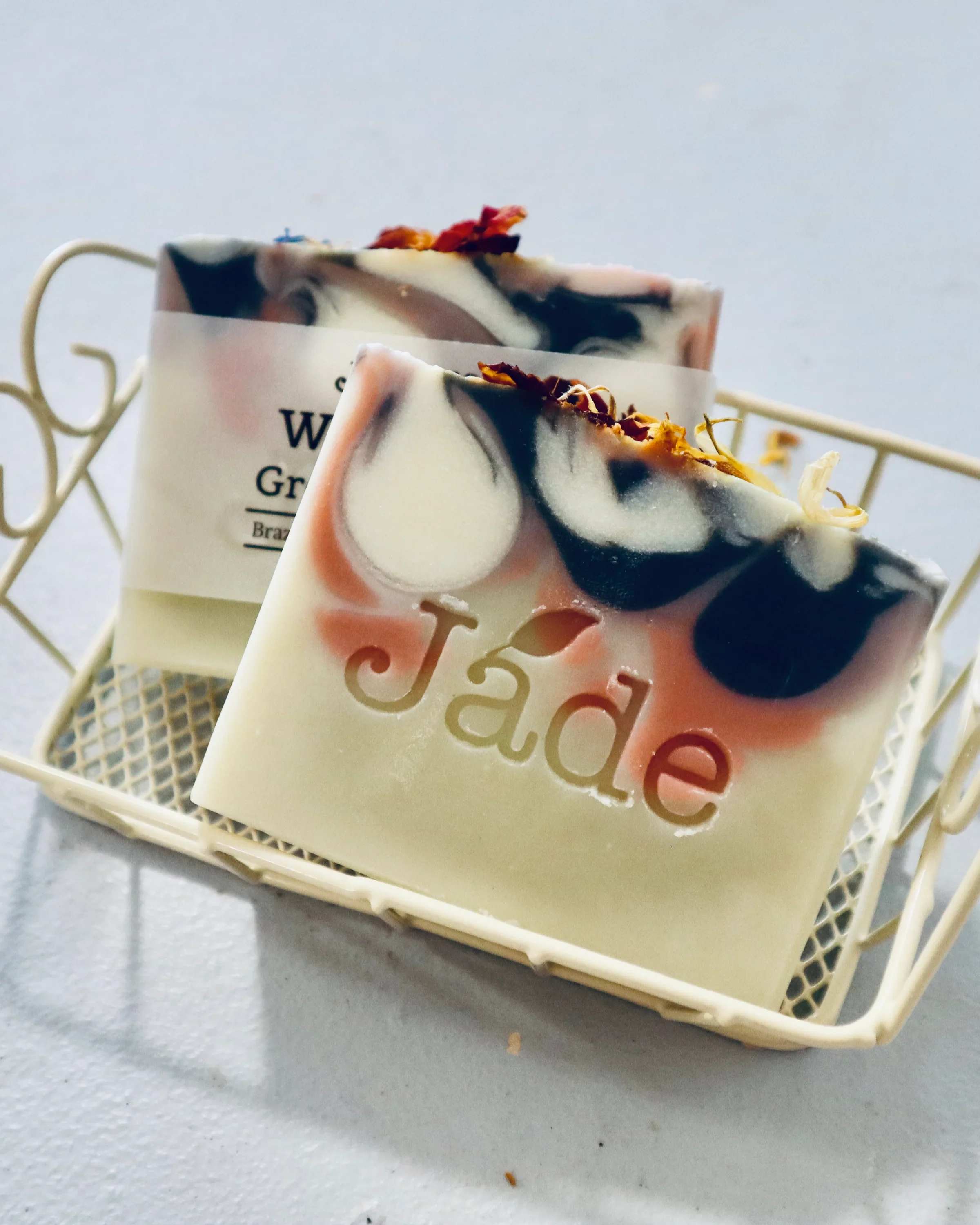 Two decorative soap bars with pink and black swirls in a small cream metal basket