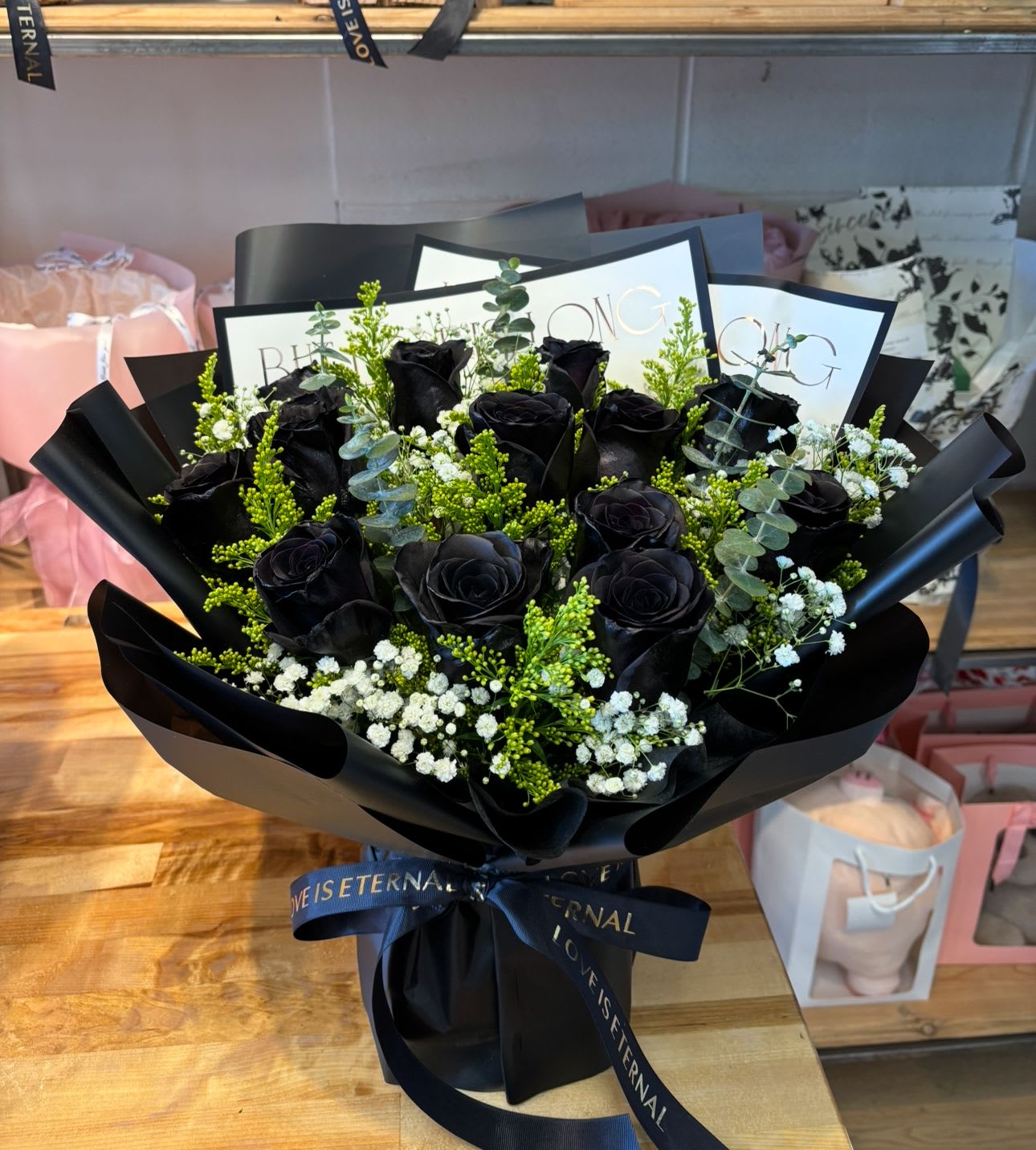 Bouquet of black roses with white filler flowers wrapped in glossy black paper and ribbon