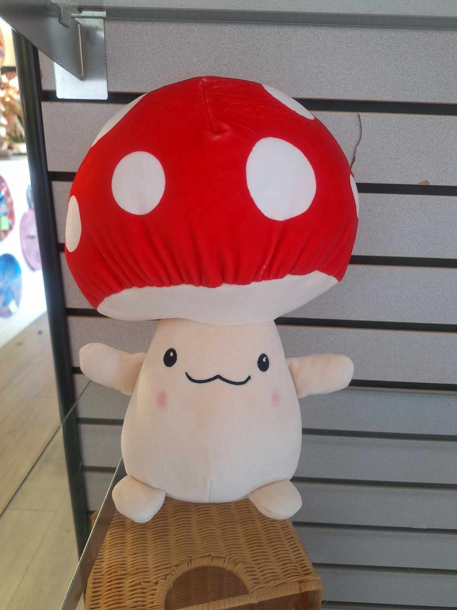 Plush mushroom toy with a red polka-dot cap and smiling face displayed on a shelf