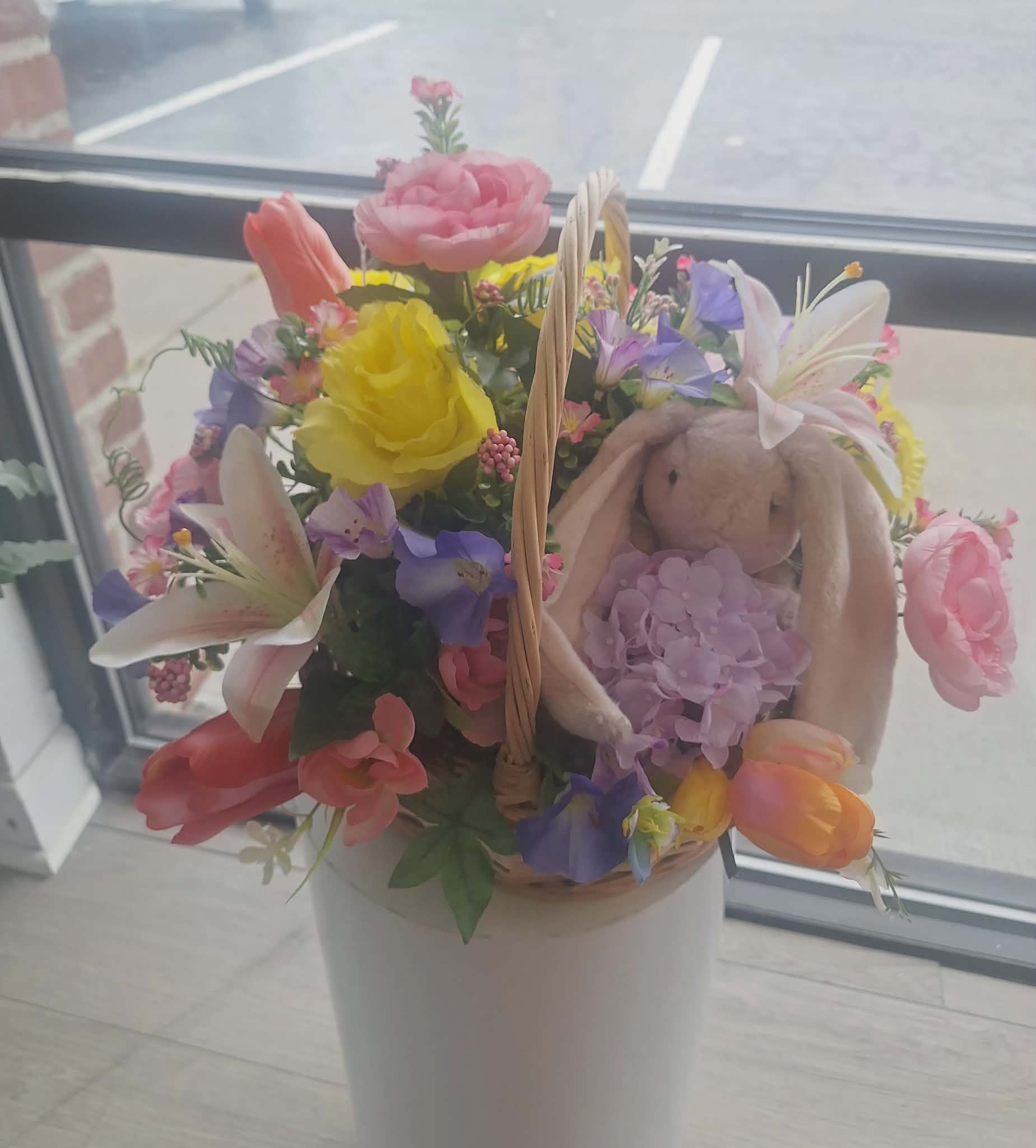 Basket of mixed pink, yellow, and purple flowers with a plush bunny tucked among the blooms