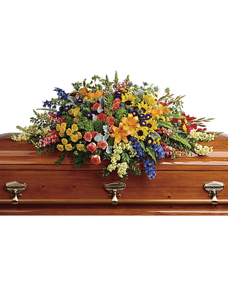 Colorful casket spray of mixed flowers in yellow, orange, blue, and pink atop a wooden casket.