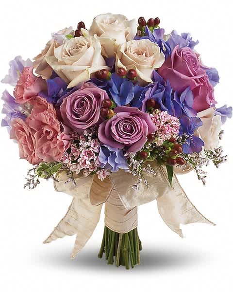 Hand-tied bouquet of ivory and lavender roses with pink blooms and blue flowers wrapped in an ivory ribbon