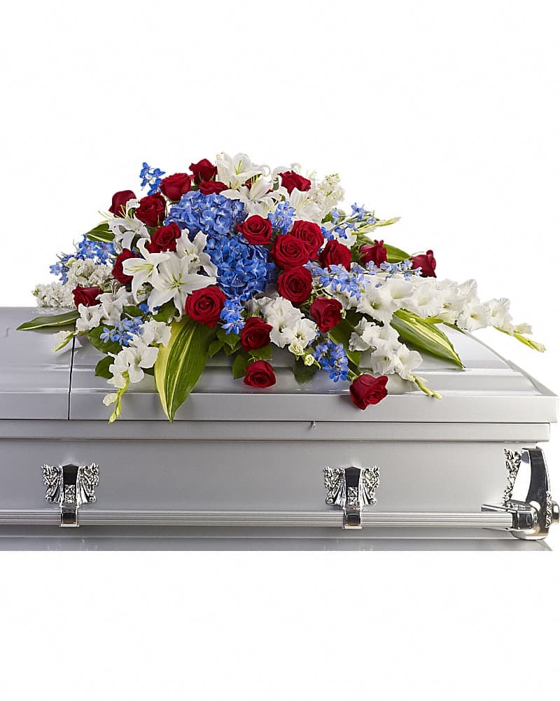 Red, white, and blue floral casket spray with roses, lilies, and hydrangeas on a silver casket