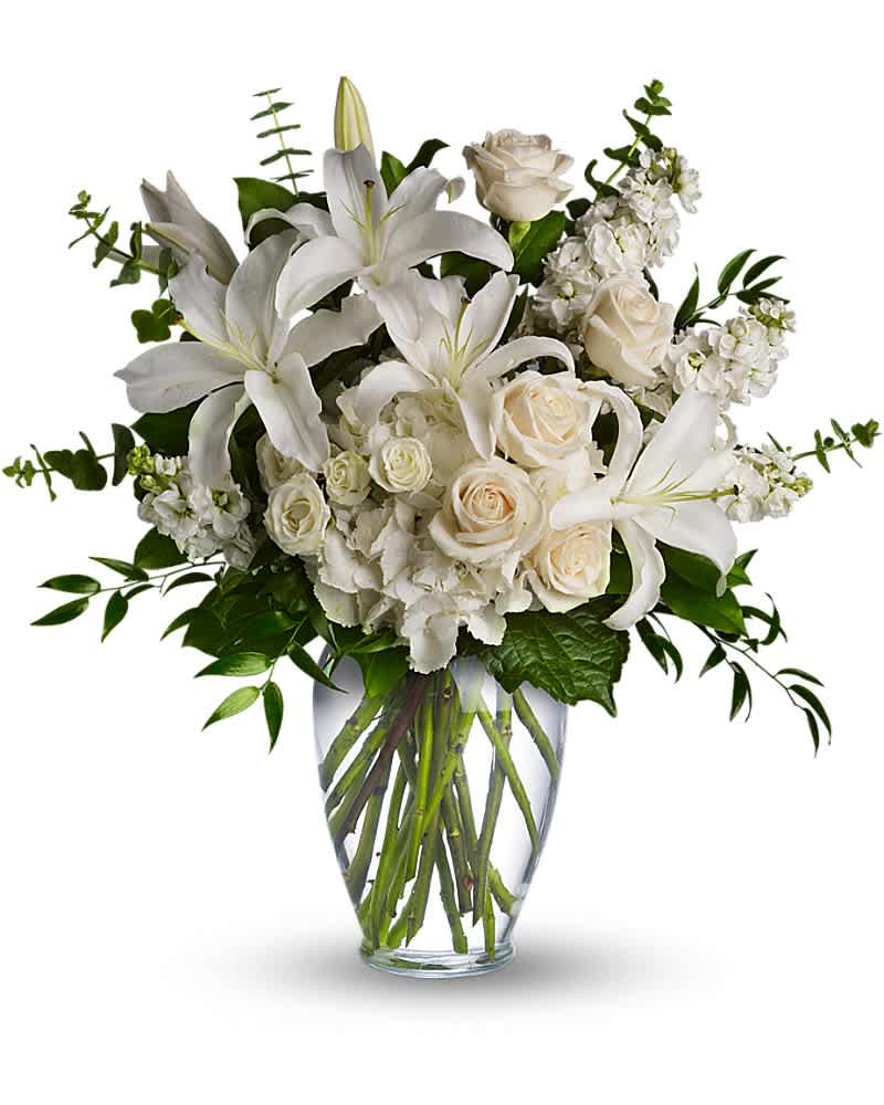 White lilies, roses, and hydrangeas arranged in a clear glass vase with visible stems.