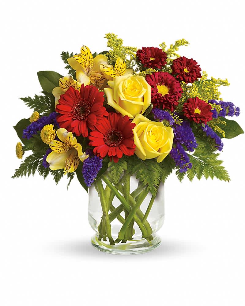 Bright bouquet of yellow roses, red gerbera daisies, and mixed blooms in a clear glass vase