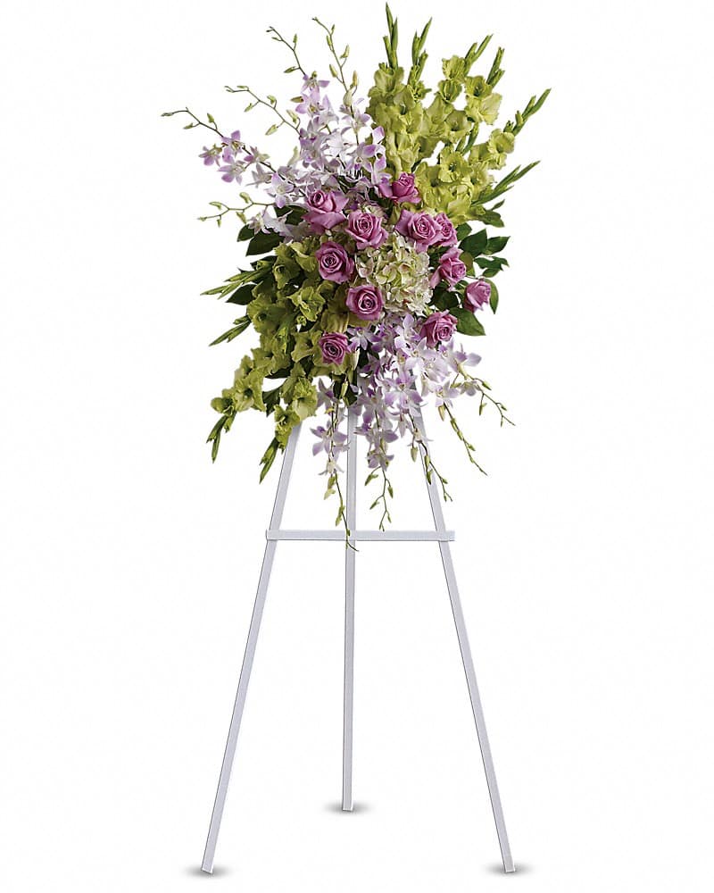 Standing spray with lavender roses, white orchids, and green flowers on a white easel