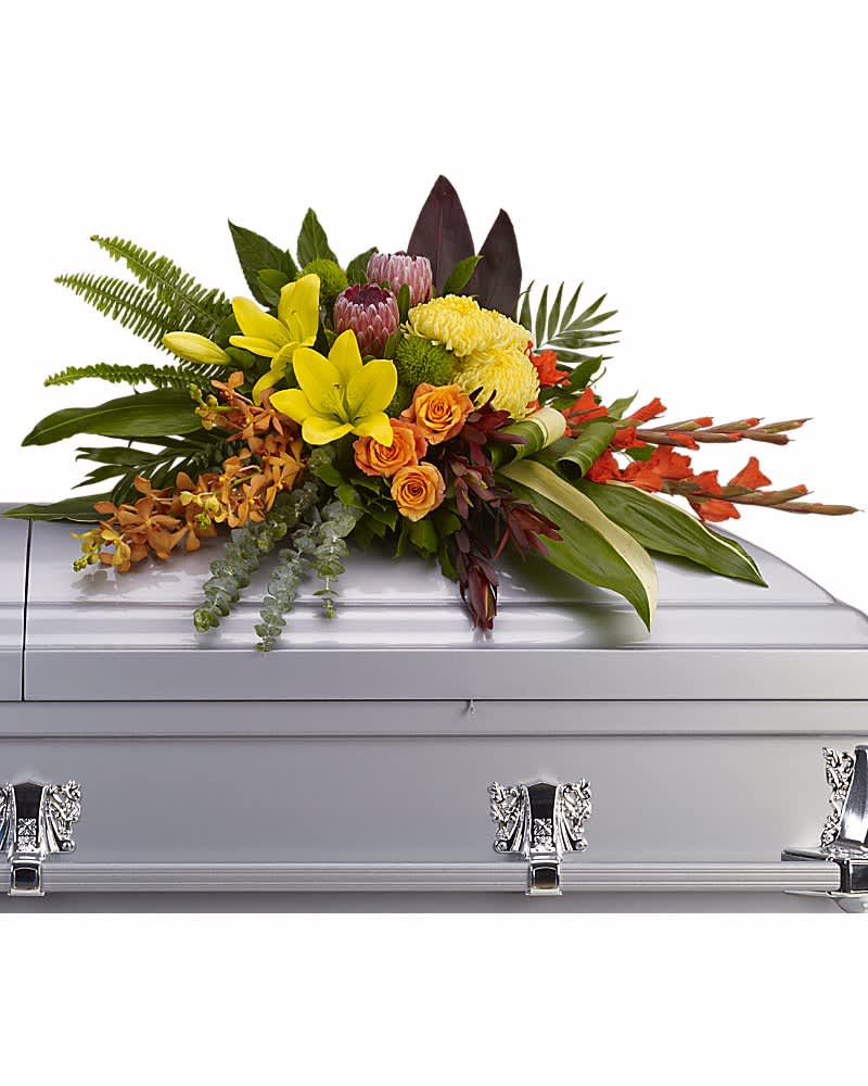Tropical casket spray of yellow lilies, orange roses, orchids, and protea on a silver casket.