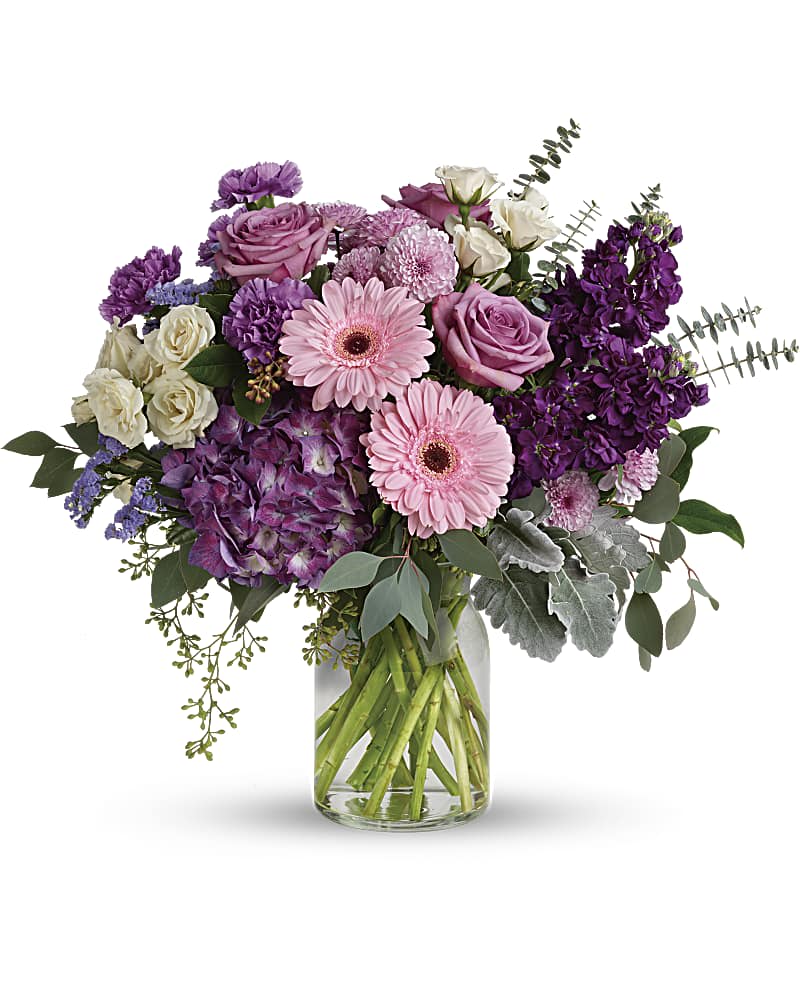 Mixed bouquet of pink gerbera daisies, purple roses, and hydrangea in a clear glass vase