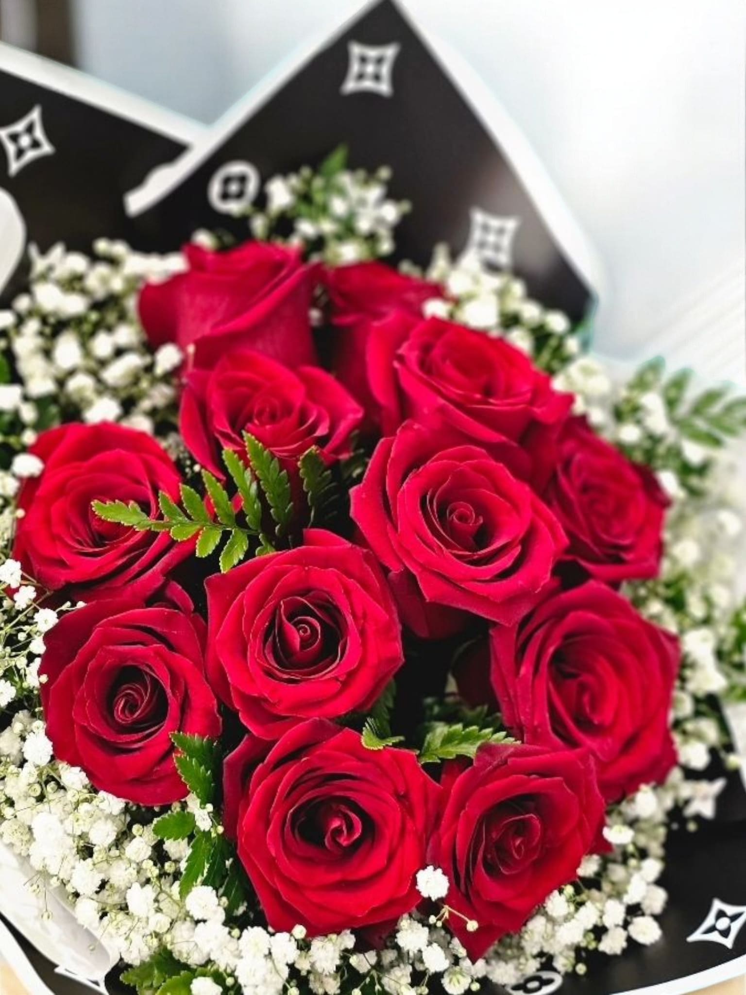 12 Red Roses Bouquet - This elegant bouquet features 12 beautiful red roses and delicate white gypsophila, wrapped in luxurious black paper. The perfect expression of love and passion, these roses are carefully selected for their quality and beauty. Surprise your loved one with this stunning arrangement today.
