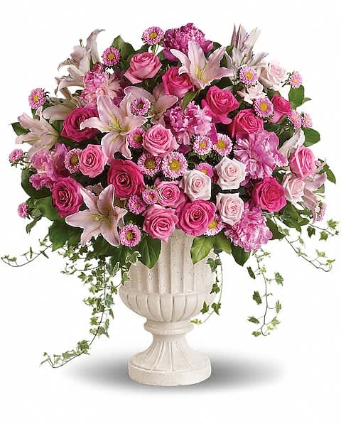 Large pink and white arrangement of roses and lilies in a white urn-style vase with trailing ivy