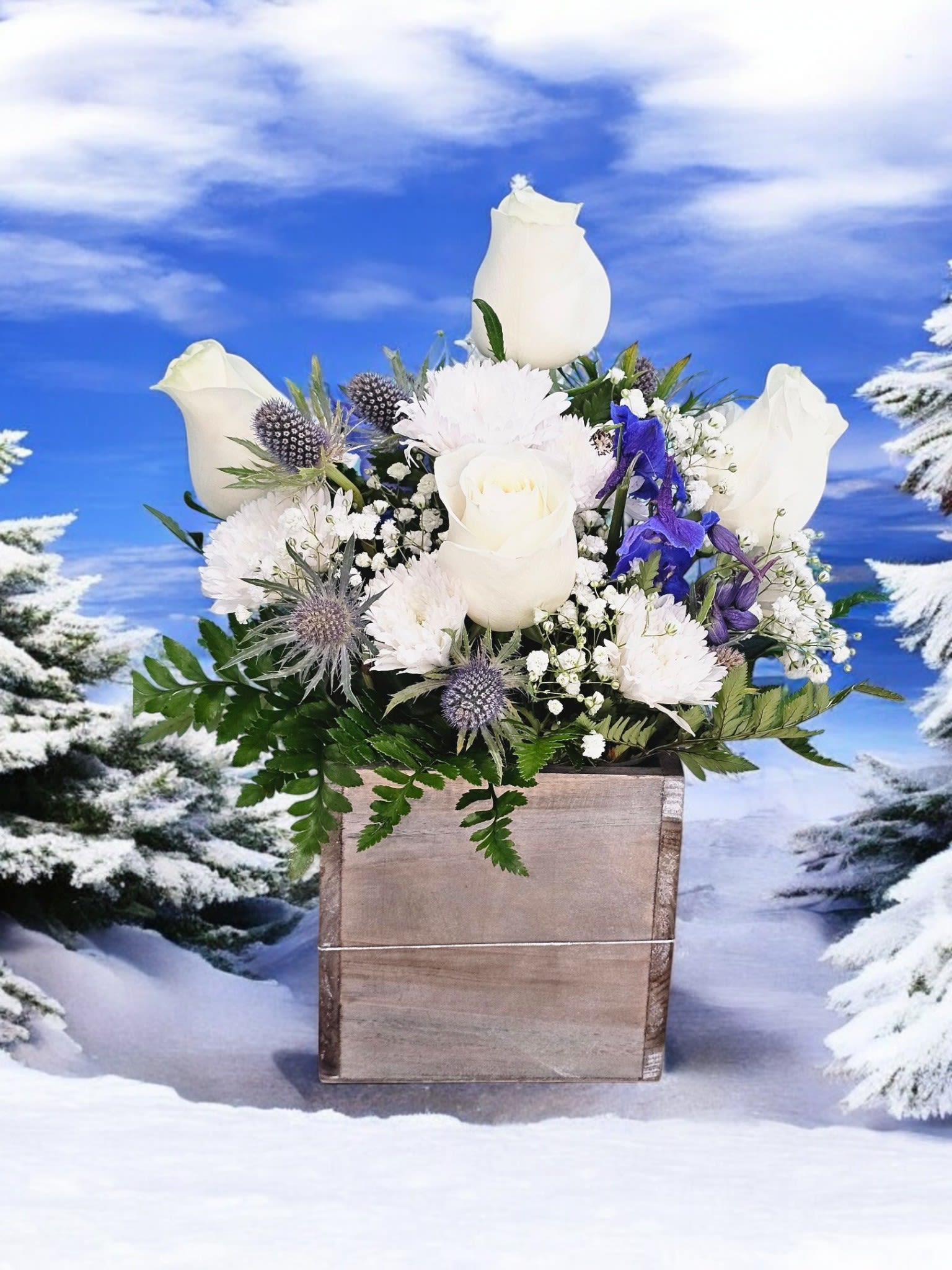 Arctic Whisper - This elegant arrangement features white roses and delicate blue delphinium against a bed of white cushion and gypsophilia, all placed in a charming woodcube design. The perfect choice for any occasion, the Arctic Whisper adds a touch of sophistication and serenity to any room.