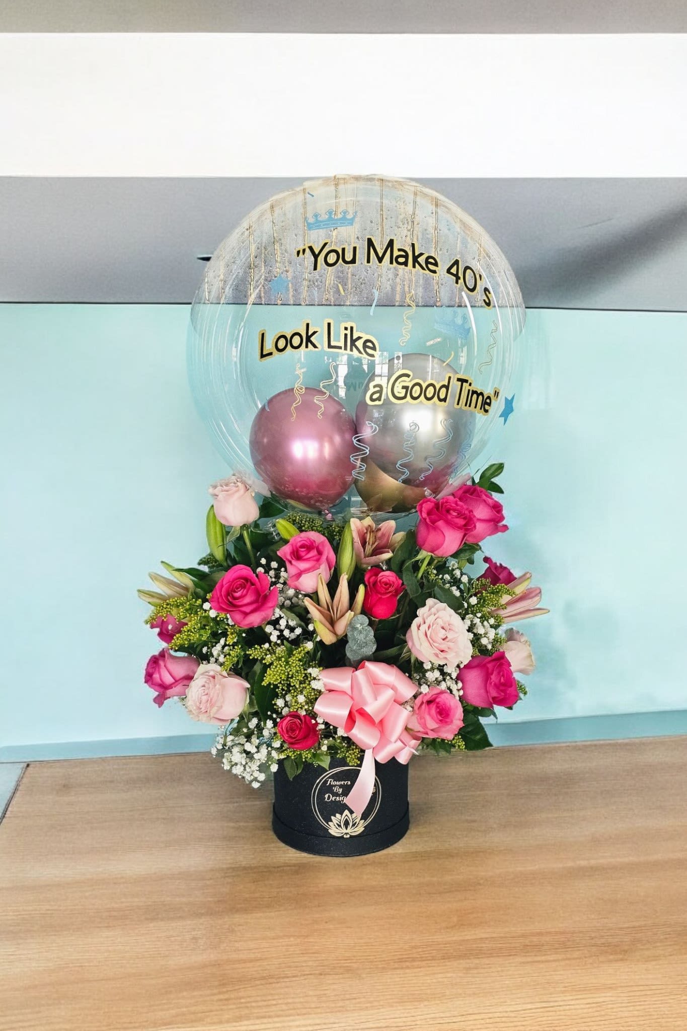 Chic Blossom Celebration - This name highlights both the elegance of the black box and the vibrant, luxurious nature of the floral arrangement and balloon. This Arrangement is made with Light Pink Roses, Hot Pink Roses, Light Pink Lilies, and Fine filler and Greenery.