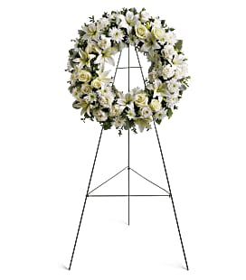 Serenity Wreath - This elegant wreath is beautifully adorned with white cushion, roses, lilies, and carnations, along with seeded eucalyptus and fine greenery. With its serene color palette and delicate floral arrangements, this wreath is the perfect way to honor a loved one's memory and bring comfort to those left behind.