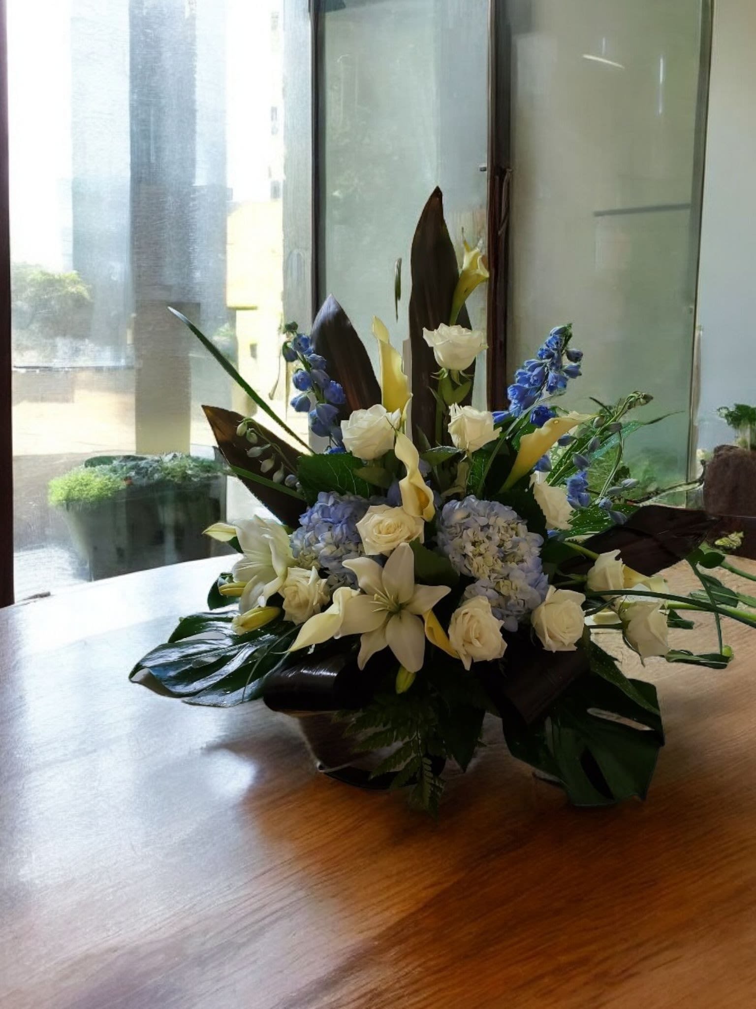 Celestial Comfort - This highlight the soothing and respectful nature of the arrangement while emphasizing the calming color palette and luxurious blooms. This Arrangement will be made with white Callas, White Roses, White lilies, Blue Delphinium, Blue Hydrengas, and assorted tropical Greneery.