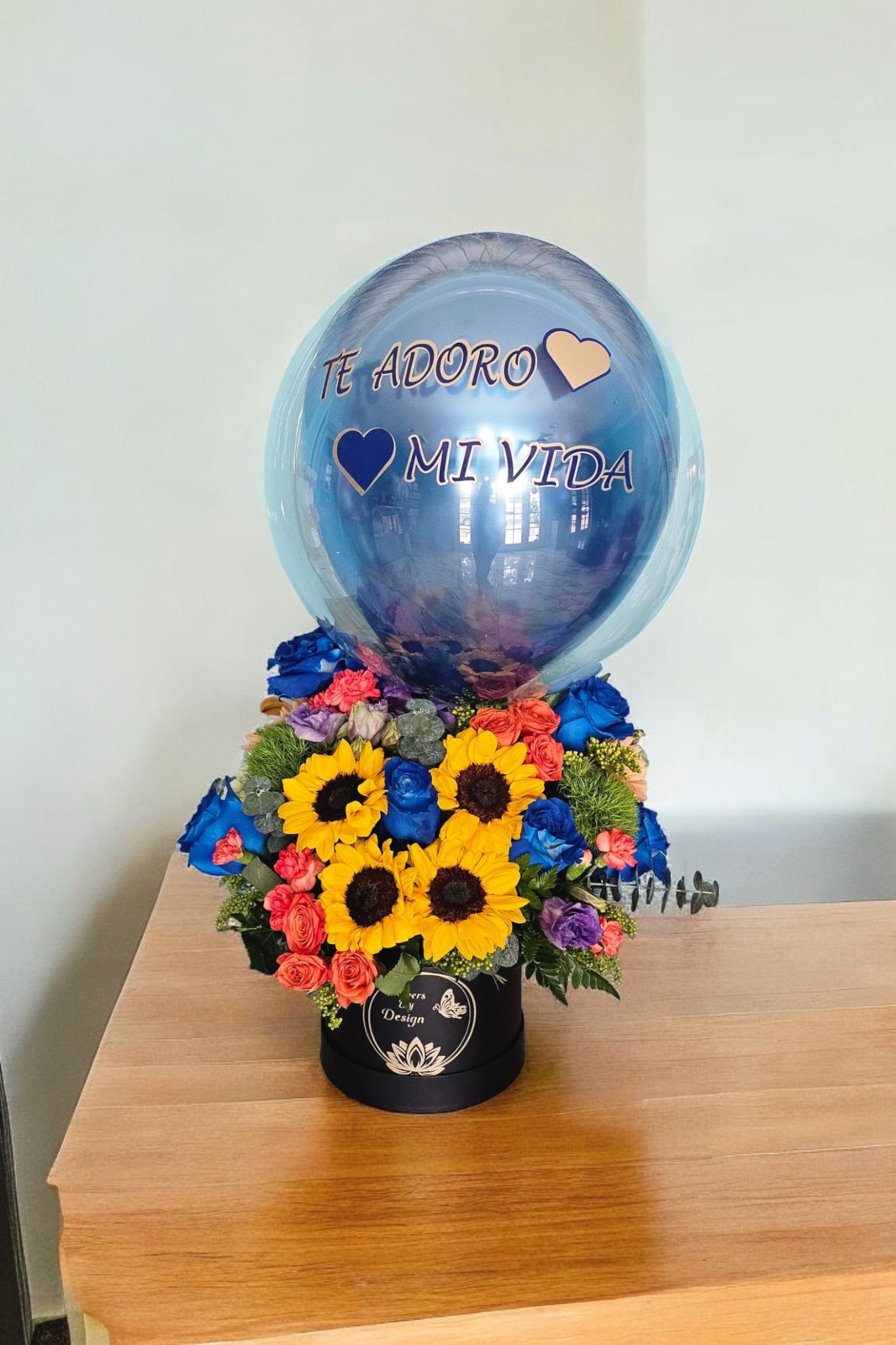 Sunset Elegance - This stunning arrangement features bright sunflowers, blue roses, orange gerberas, and other colorful blooms in an elegant box. Personalize it with a customized balloon for a truly unique gift. Perfect for any occasion and guaranteed to bring a smile to your loved one's face.