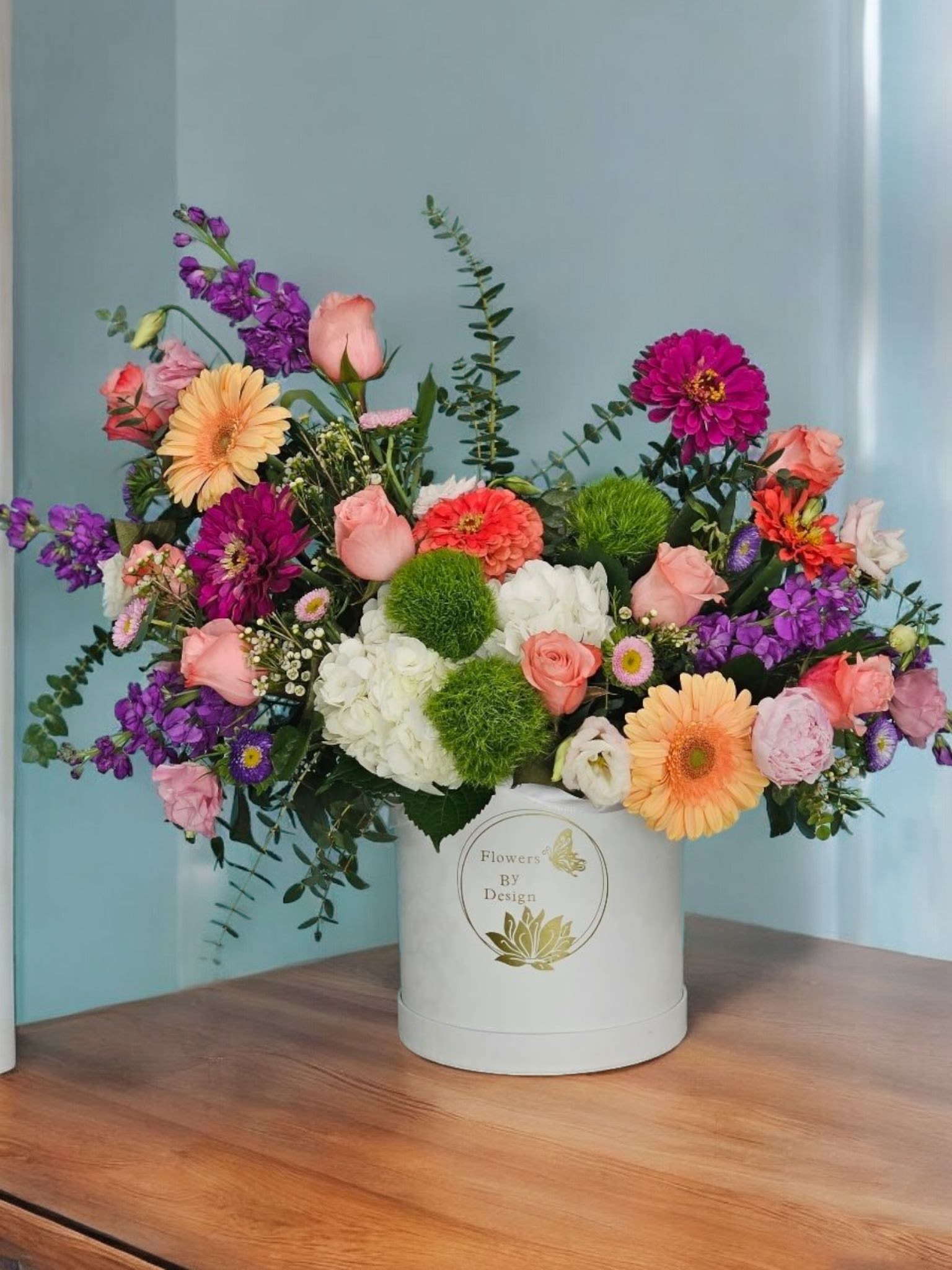 Blush Garden Symphony - This Arrangement Captures the harmonious blend of colors and textures. It highlights the vibrant hot pink dahlias, peach gerberas, lavender stock, pink lisianthus, pink Matsumoto, white hydrangeas, light pink roses, purple Matsumoto, green trick, and complementing greenery and fine filler. The name evokes a sense of elegance and serenity, reminiscent of a beautiful garden in full bloom inside a pristine white box.